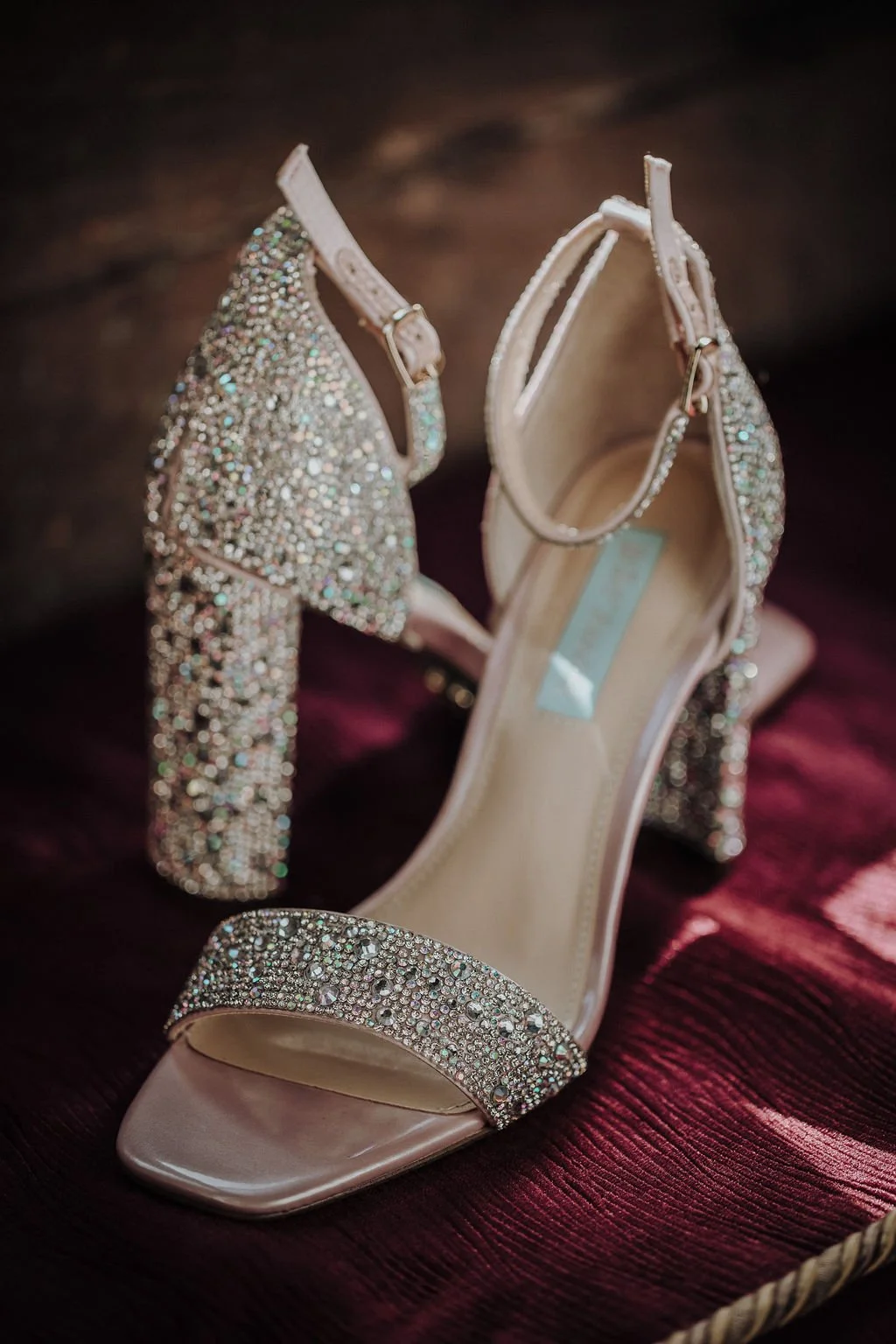 A pair of elegant, high-heeled, open-toe shoes adorned with sparkling rhinestones, resting on a dark velvet surface.