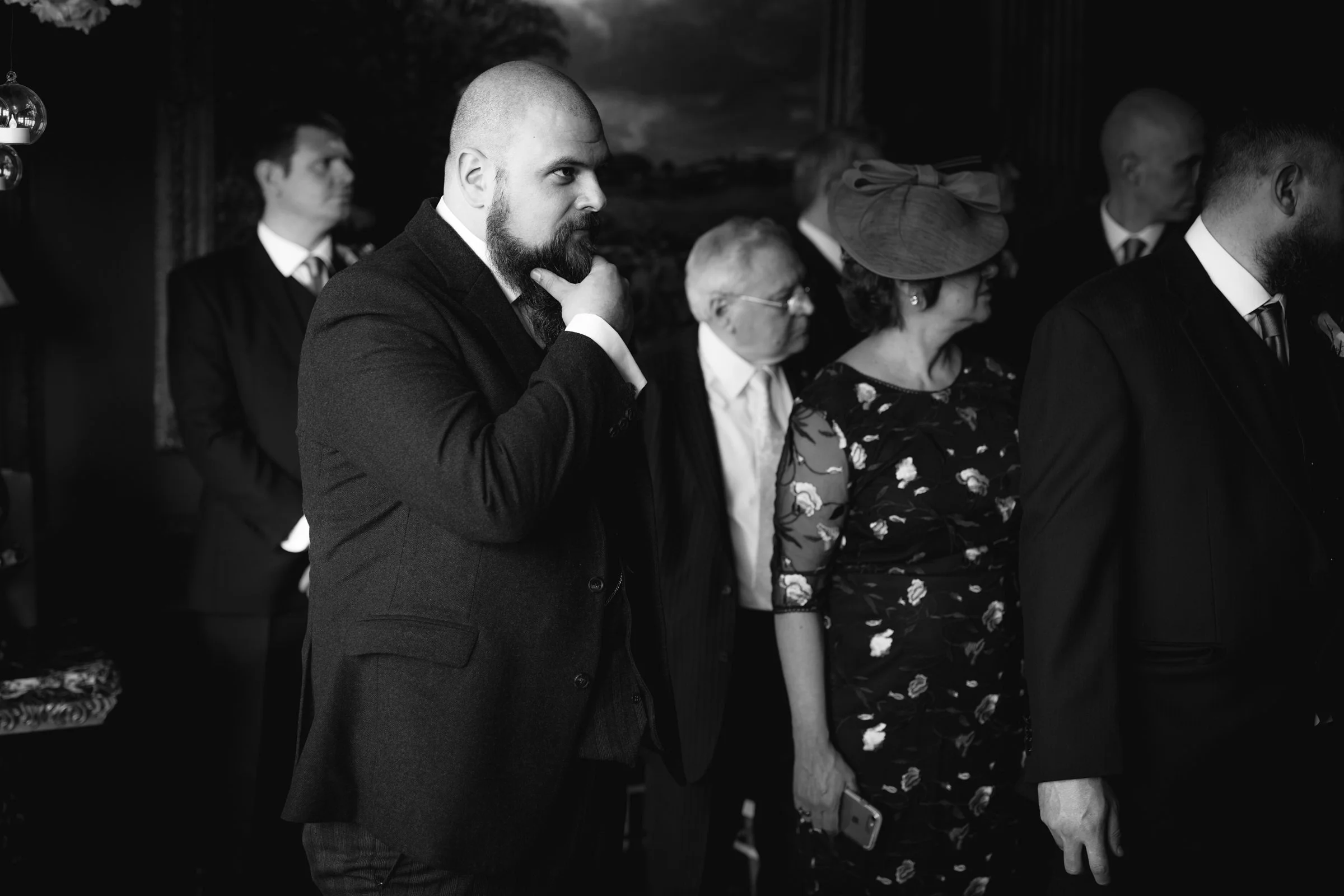 Black and white photo of well-dressed people attending a formal gathering or event, standing in a line, with some looking serious or contemplative.