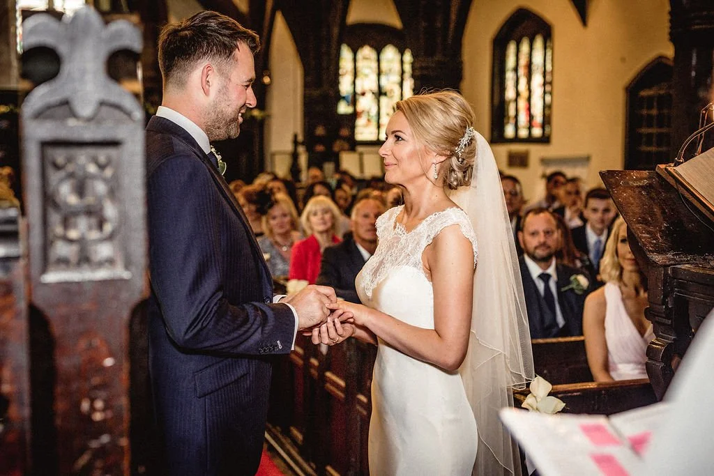 Bride and groom exchanging vows at the altar during a wedding ceremony inside a church, with guests seated in the background.