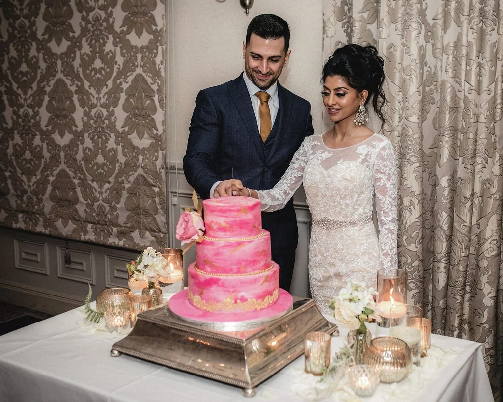 A bride and groom cutting a pink wedding cake in an elegant decorated room.