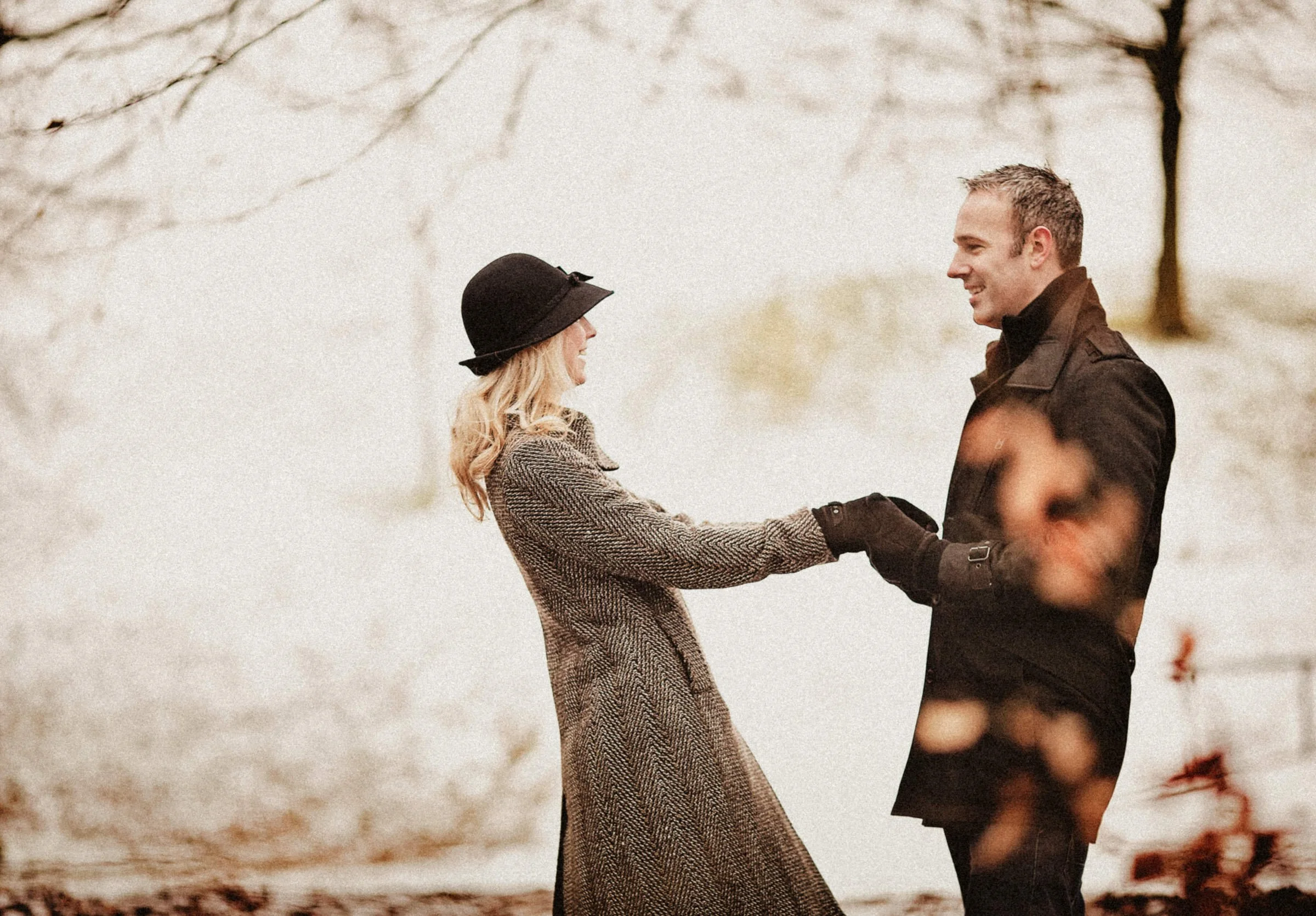 A couple holding hands and smiling at each other outdoors in a winter setting