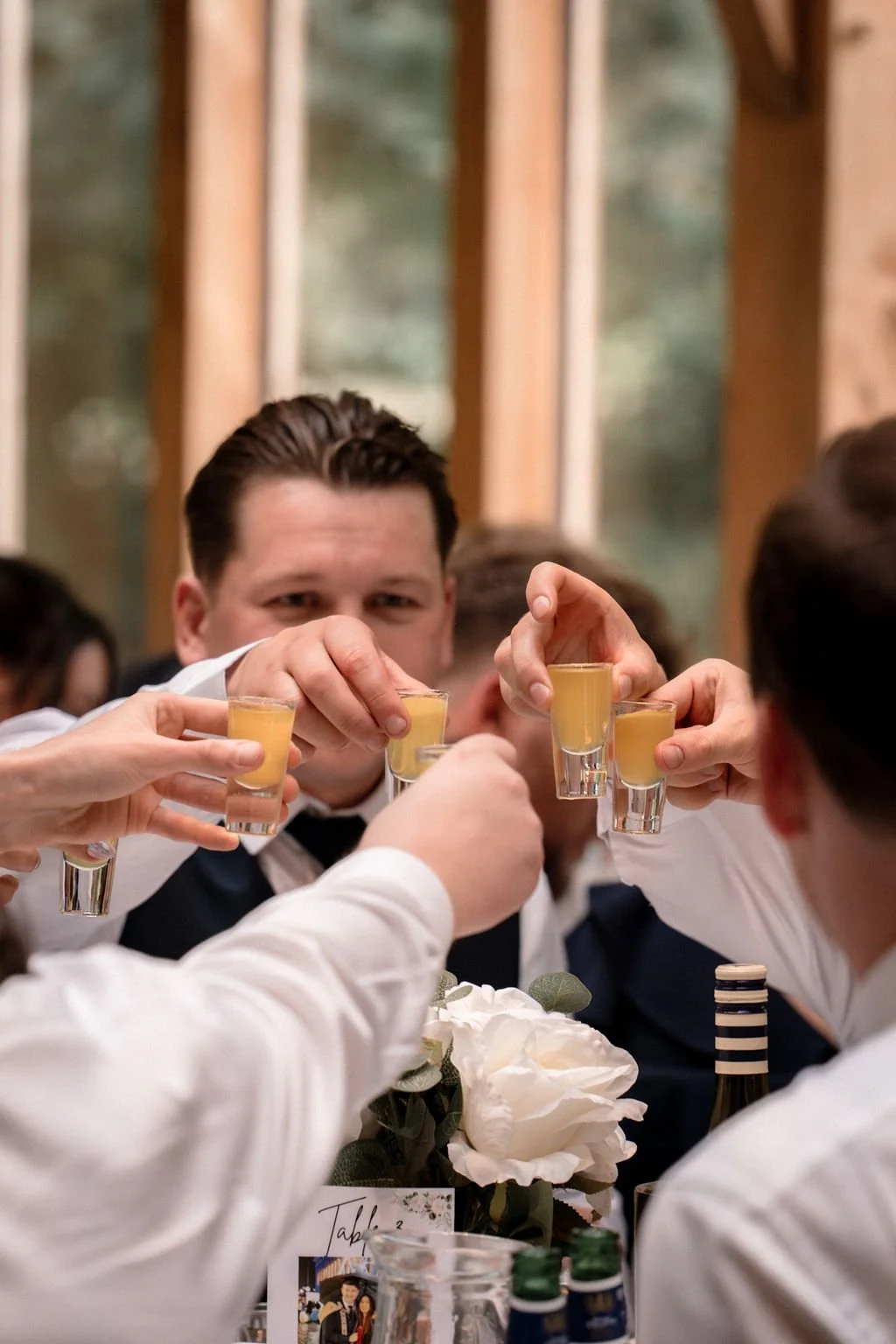 Group of people raising shot glasses of a yellow beverage in a toast during a celebration.