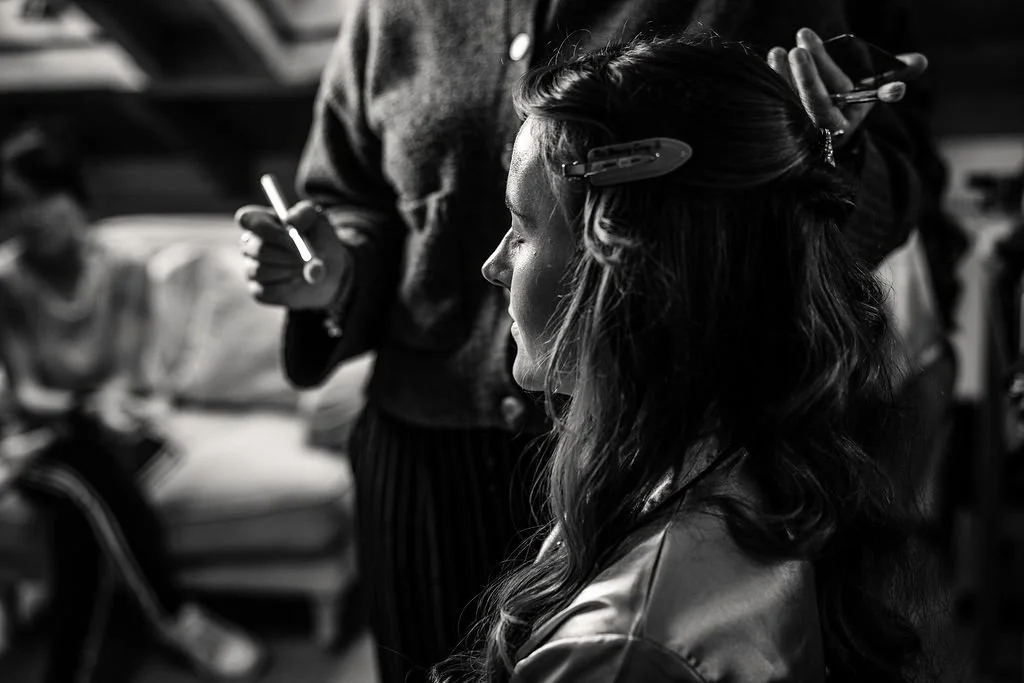 A woman getting her hair styled by a person using a hair clip and spray, in a salon setting.