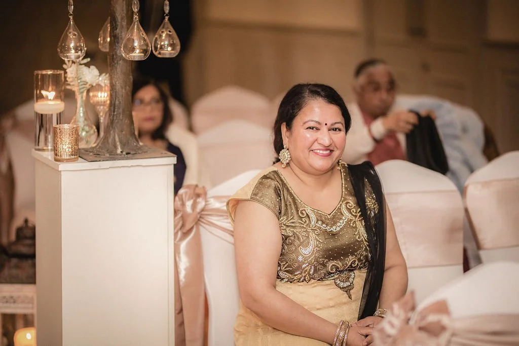 Smiling woman in Indian traditional dress sitting at a formal event with candlelit decorations nearby.