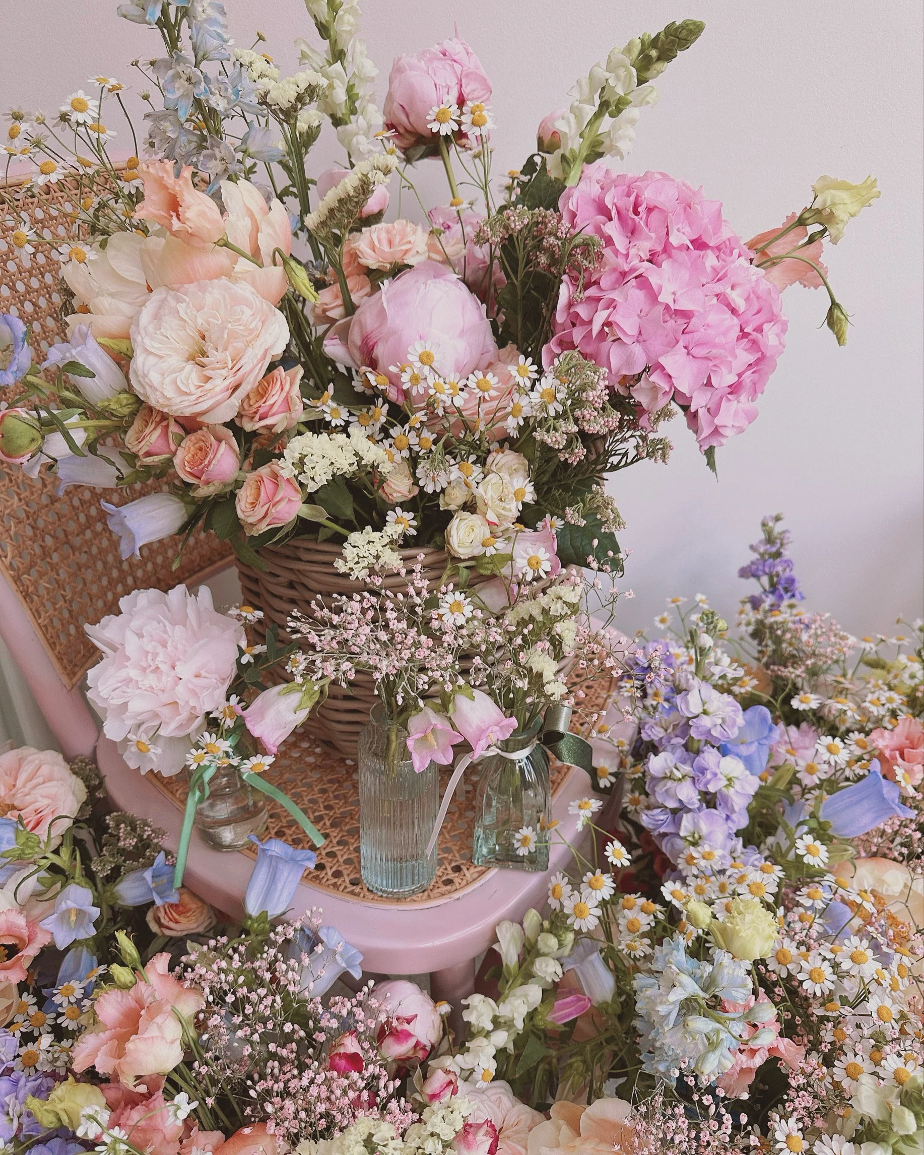 A floral arrangement with pink, white, purple, and blue flowers in glass vases on a pink chair, surrounded by additional flowers.