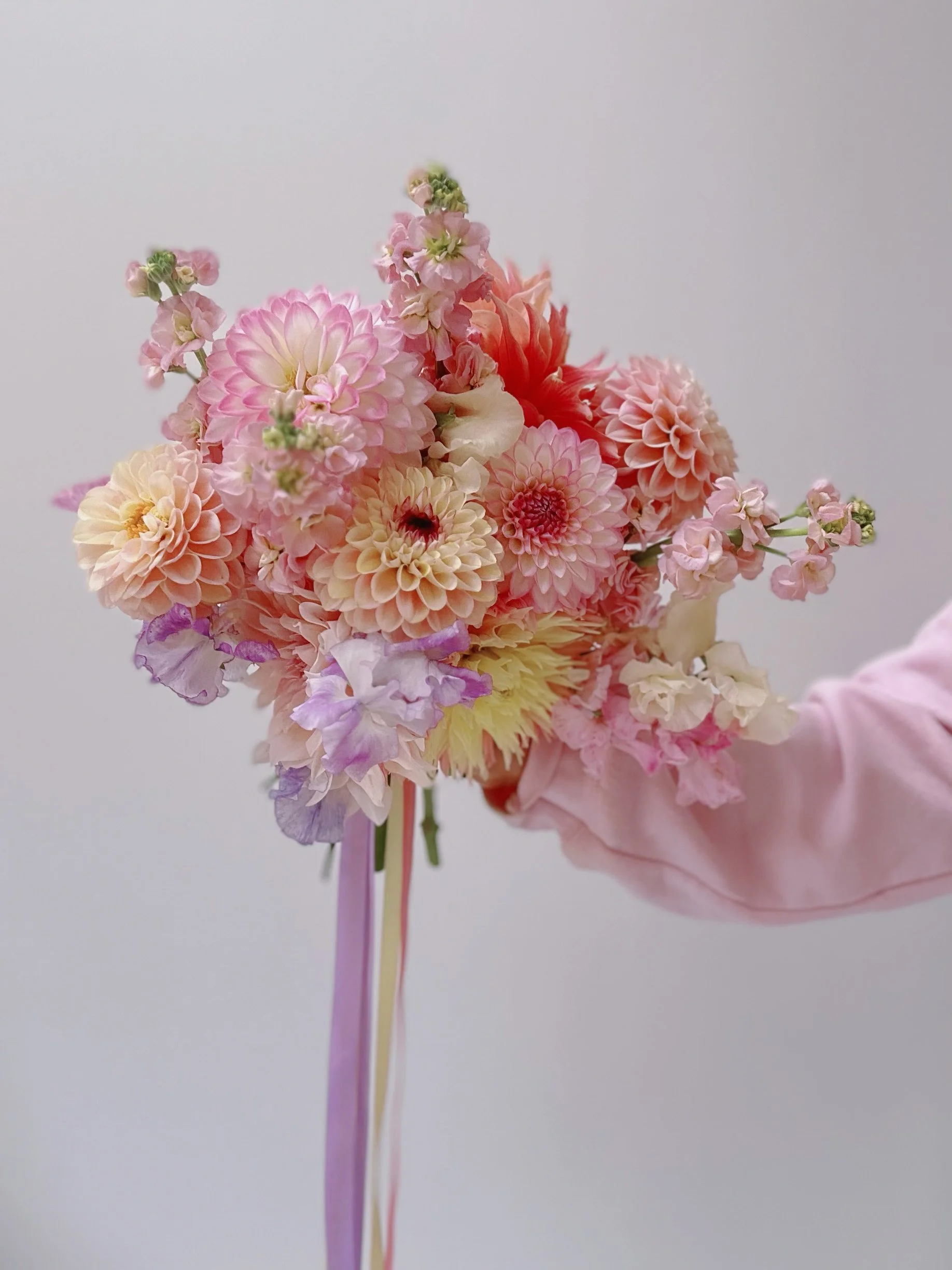 A bouquet of pink, peach, and purple flowers being held by a hand wearing a pink sleeve.