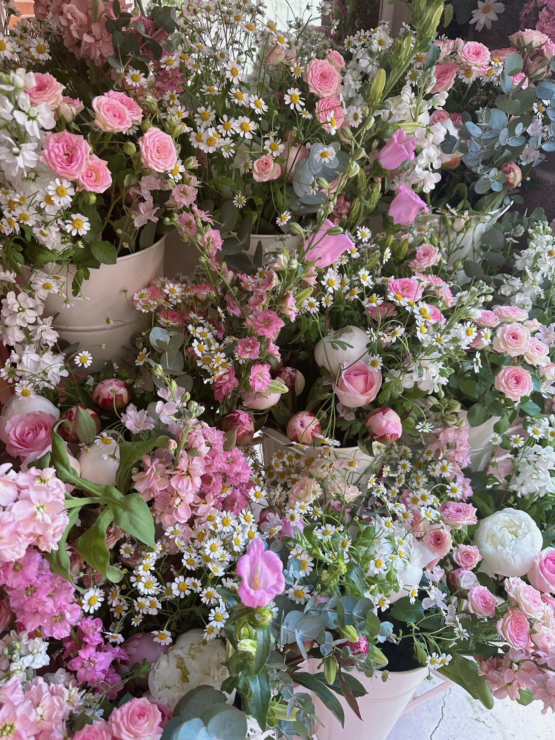 Various pink and white flowers, including roses, daisies, and peonies, arranged in pots.