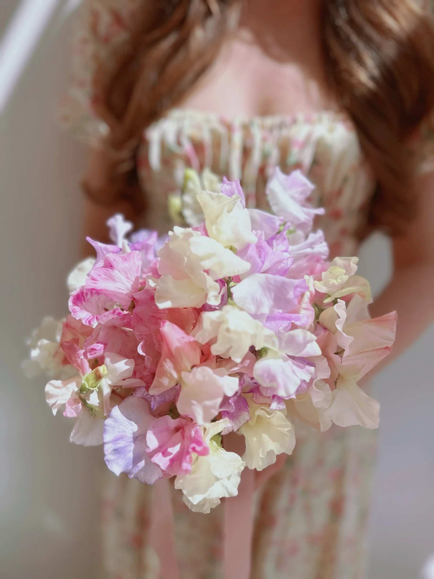 A person holding a colorful bouquet of pastel pink, purple, and white flowers, with the person's face not visible.