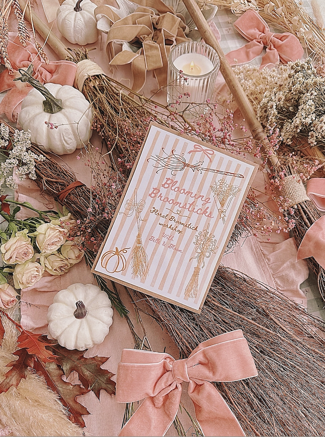 Autumn floral arrangement with pumpkins, dried branches, pink roses, leaves, pink ribbons, a candle, and a card with the text 'Blooming Bramsticks' and additional decorative elements.