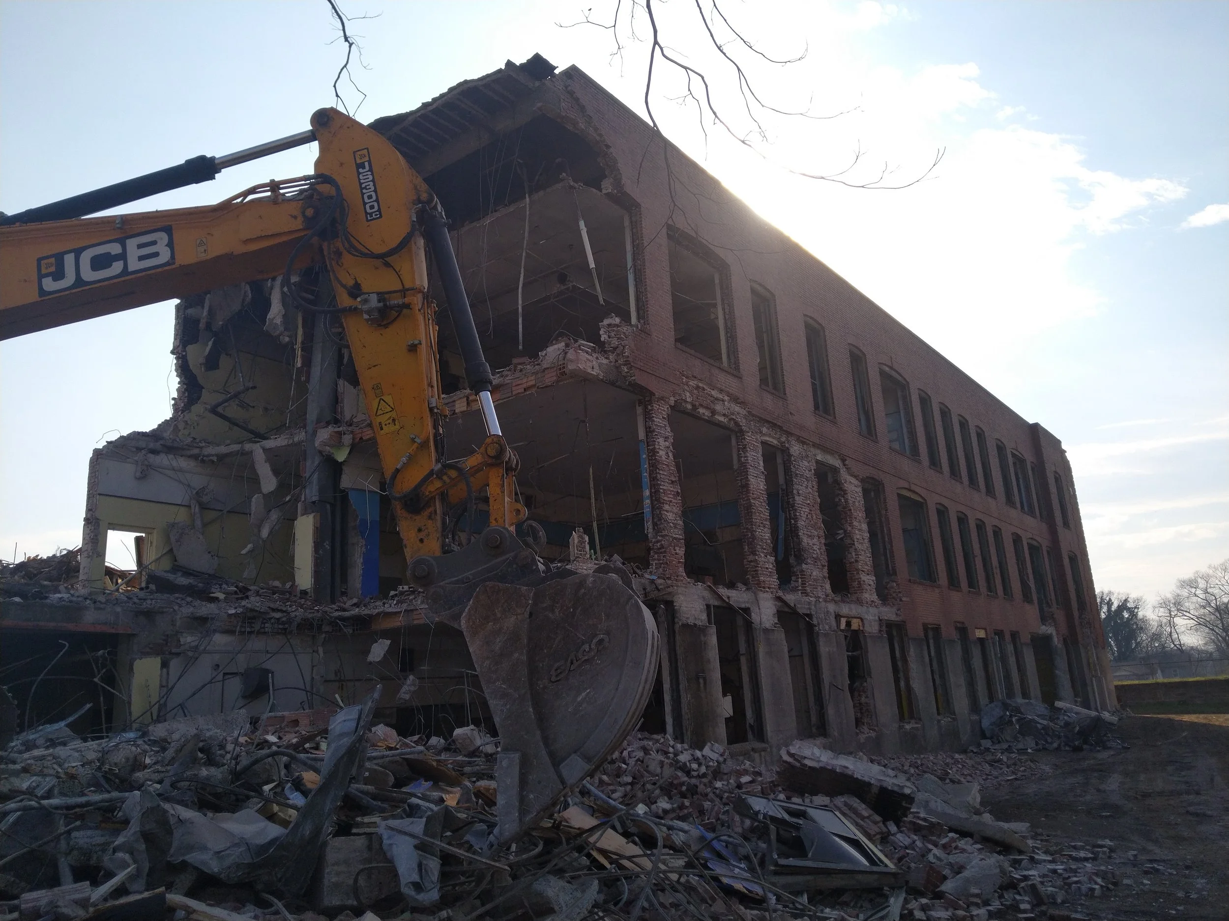 A partially demolished building with debris on the ground and an excavator destroying the structure.