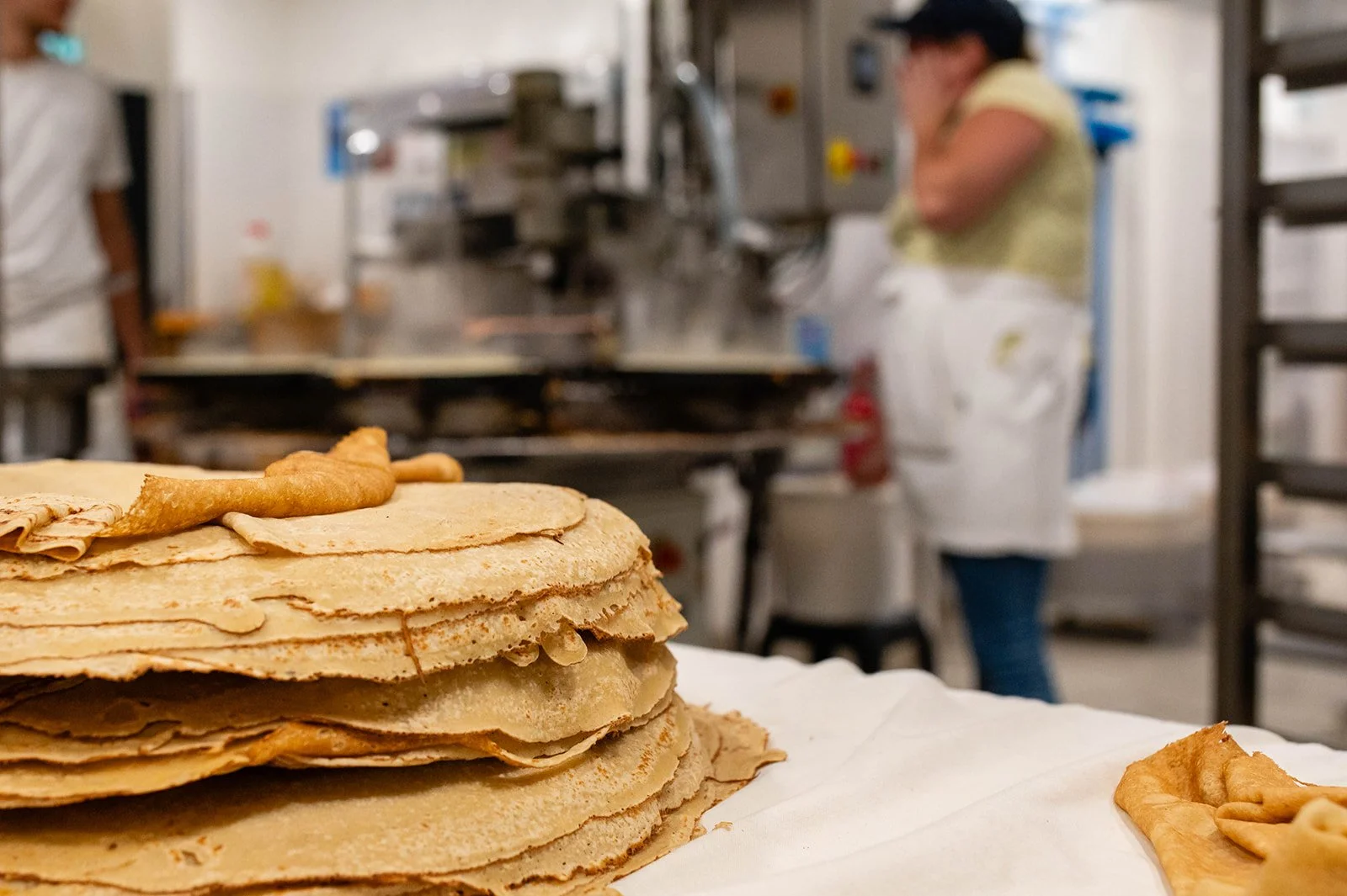 Pancakes stacked on a table in a kitchen, with a person in the background.