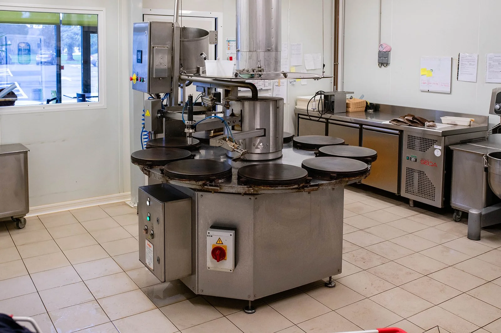 Round industrial machine used in kitchens, probably for cooking or food preparation, with a stainless steel surface, located in a professional kitchen.