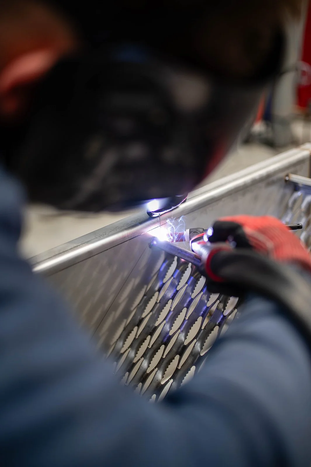 A worker welding a metal part with a welding arc, wearing protective gloves.
