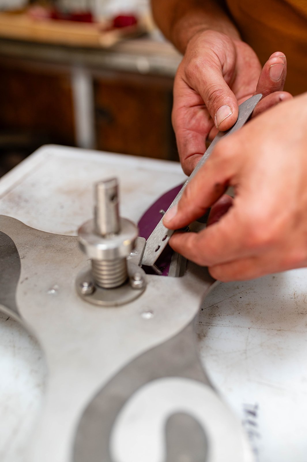 A person is using a file to polish a metal part on a workbench.