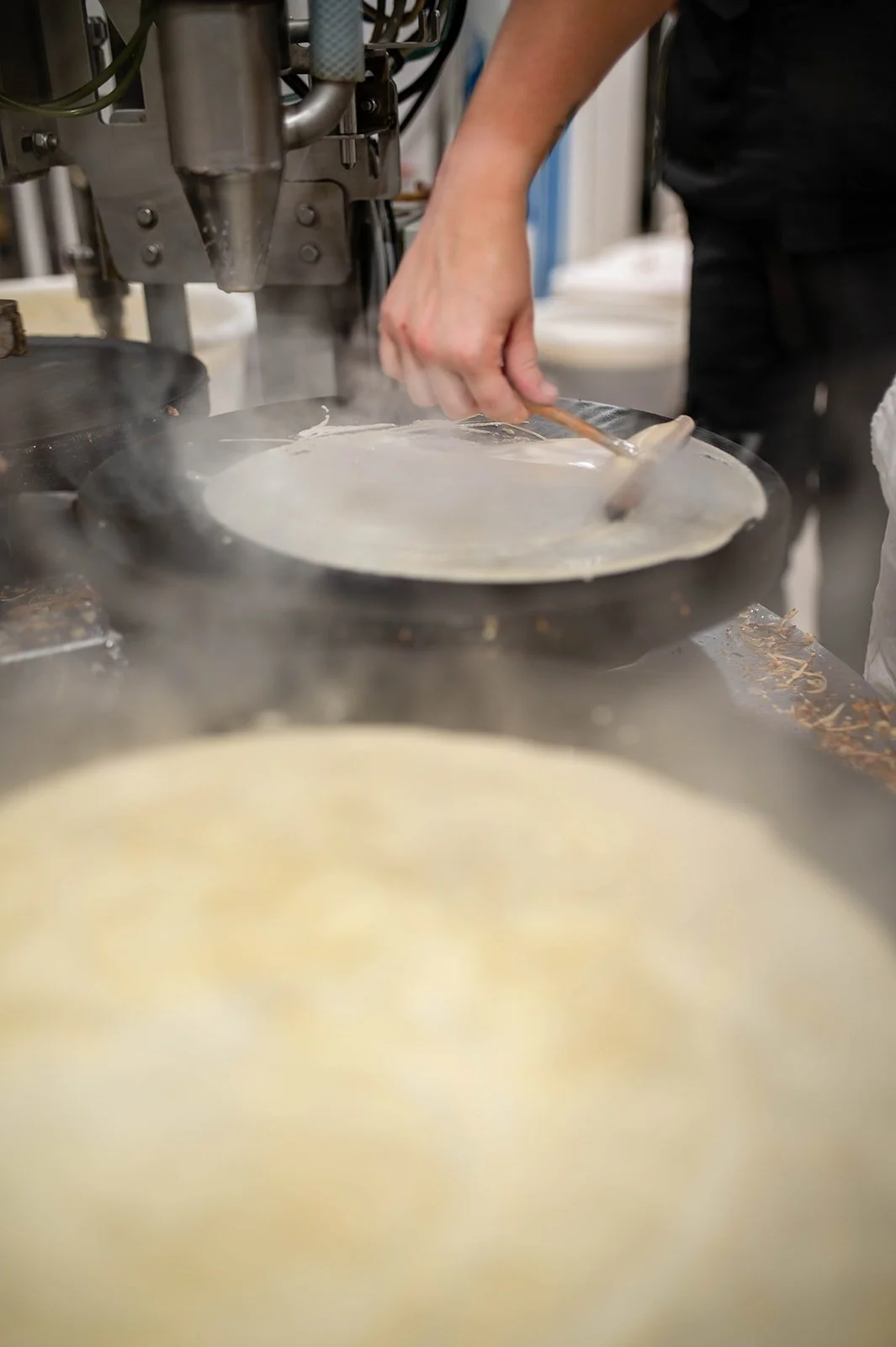 A person is preparing a pancake in a pan on a pancake machine, with pancake batter cooking.
