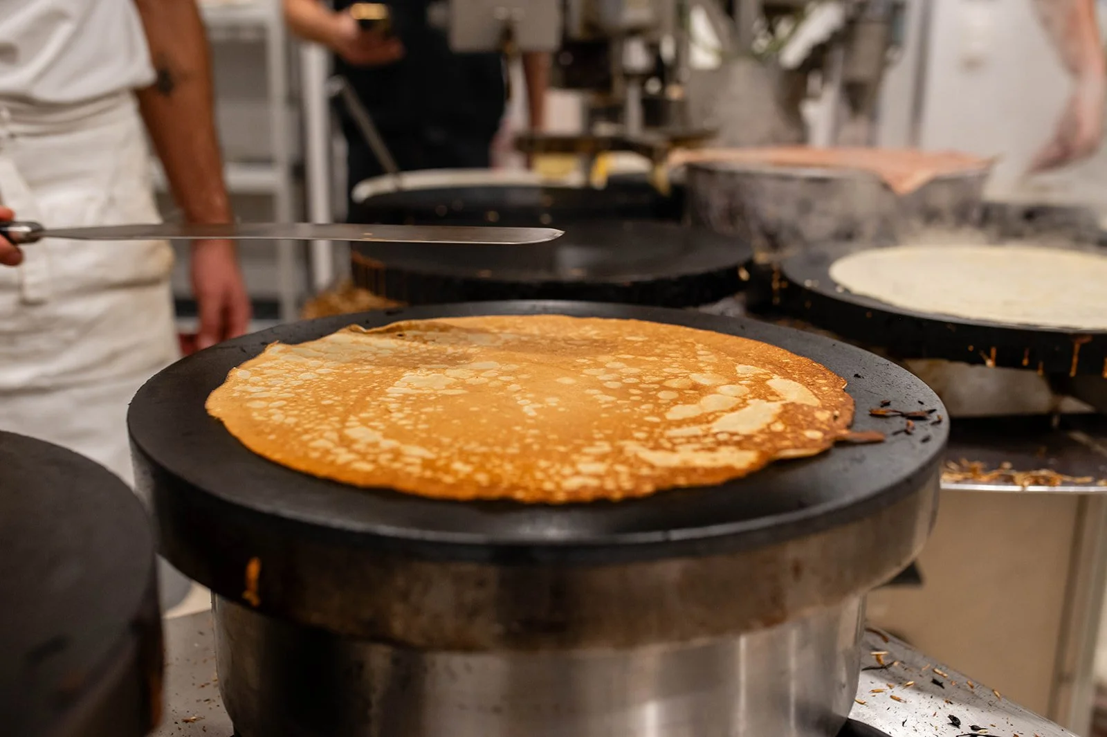 Crepes cooking on a hot plate in a kitchen.