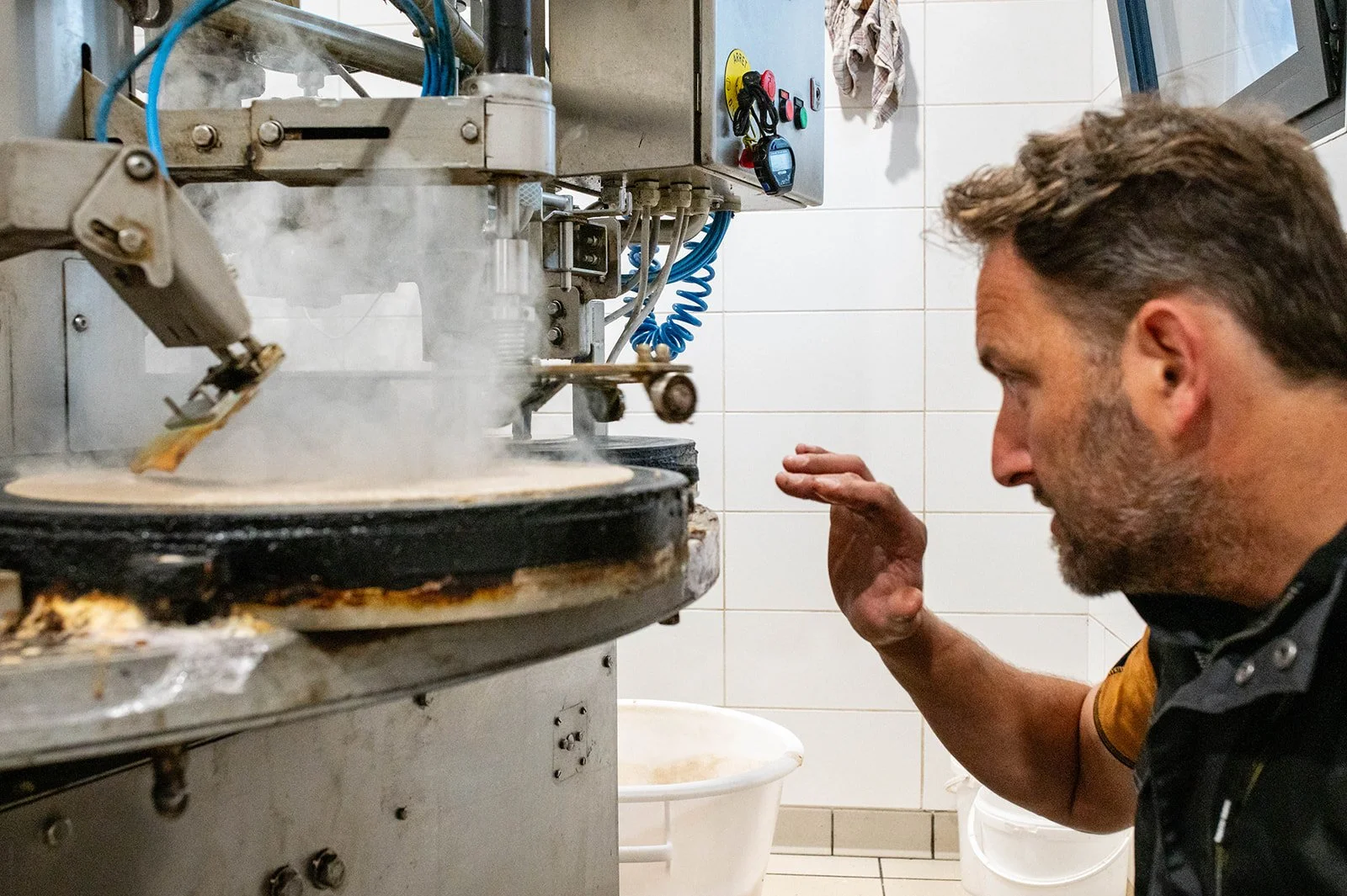 Un homme regarde une machine à crêpes en train de faire des crêpes, dans une cuisine