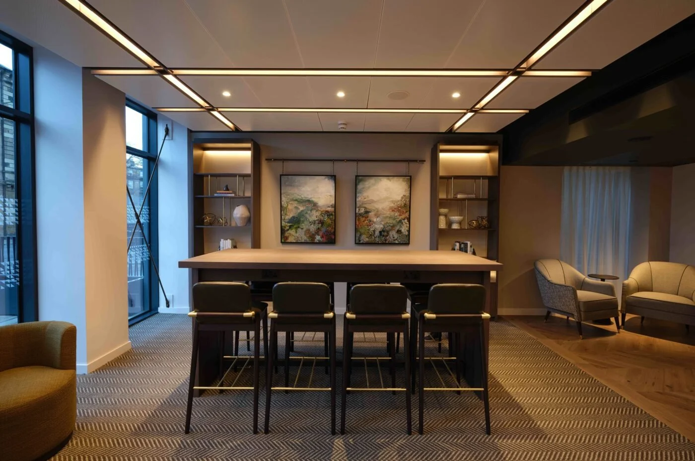 Modern living area with large windows, a high-top table designed and made by Foundry Studio with four black chairs, beige armchairs, and abstract paintings on the wall.