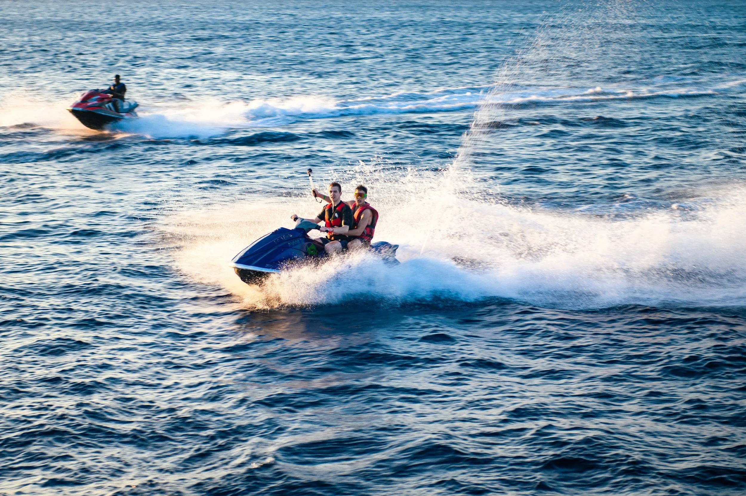 Two people riding a jet ski on the water with another jet ski in the background.
