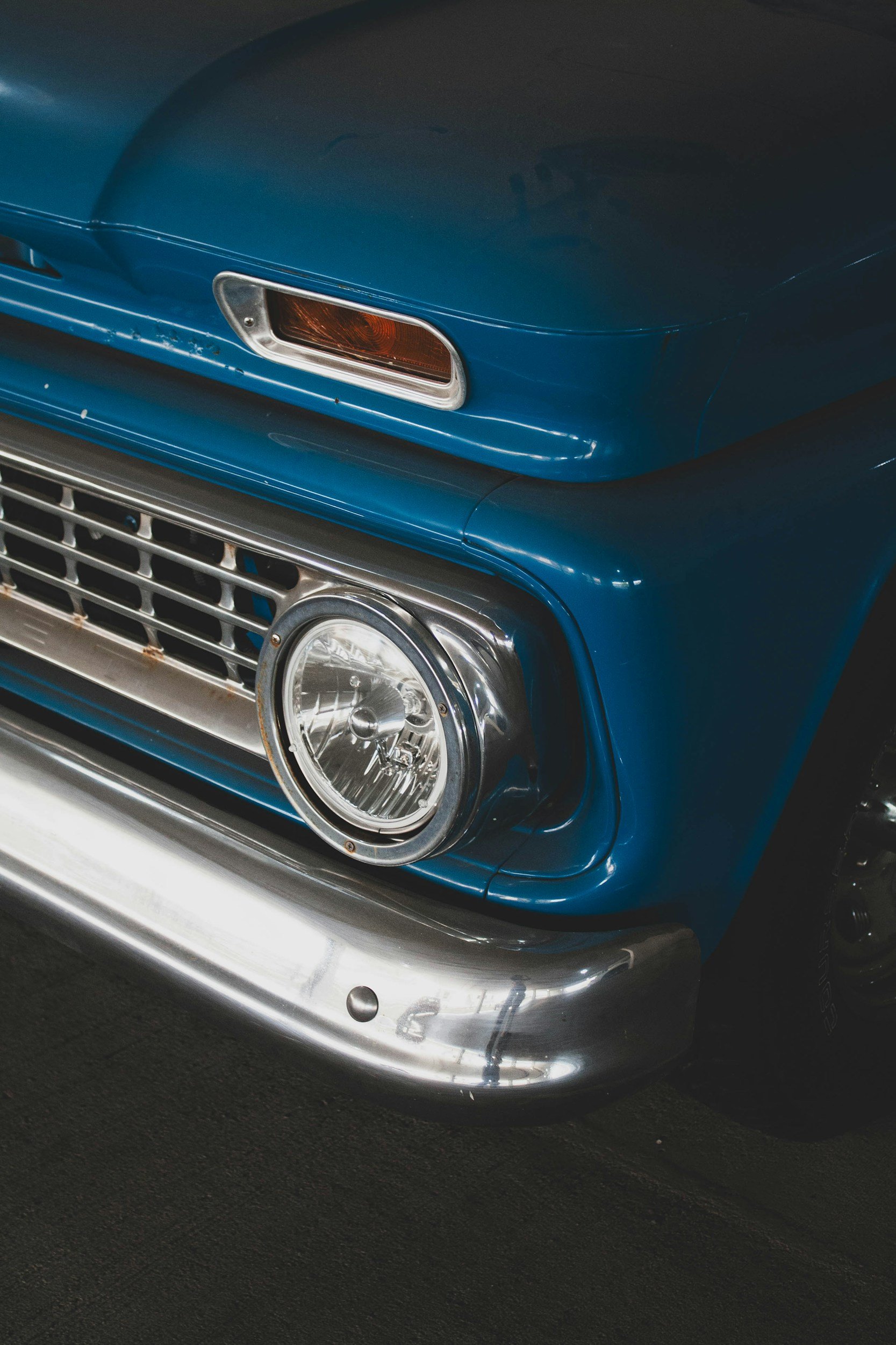 Close-up image of a vintage blue car's front, showing headlight, grille, and bumper.