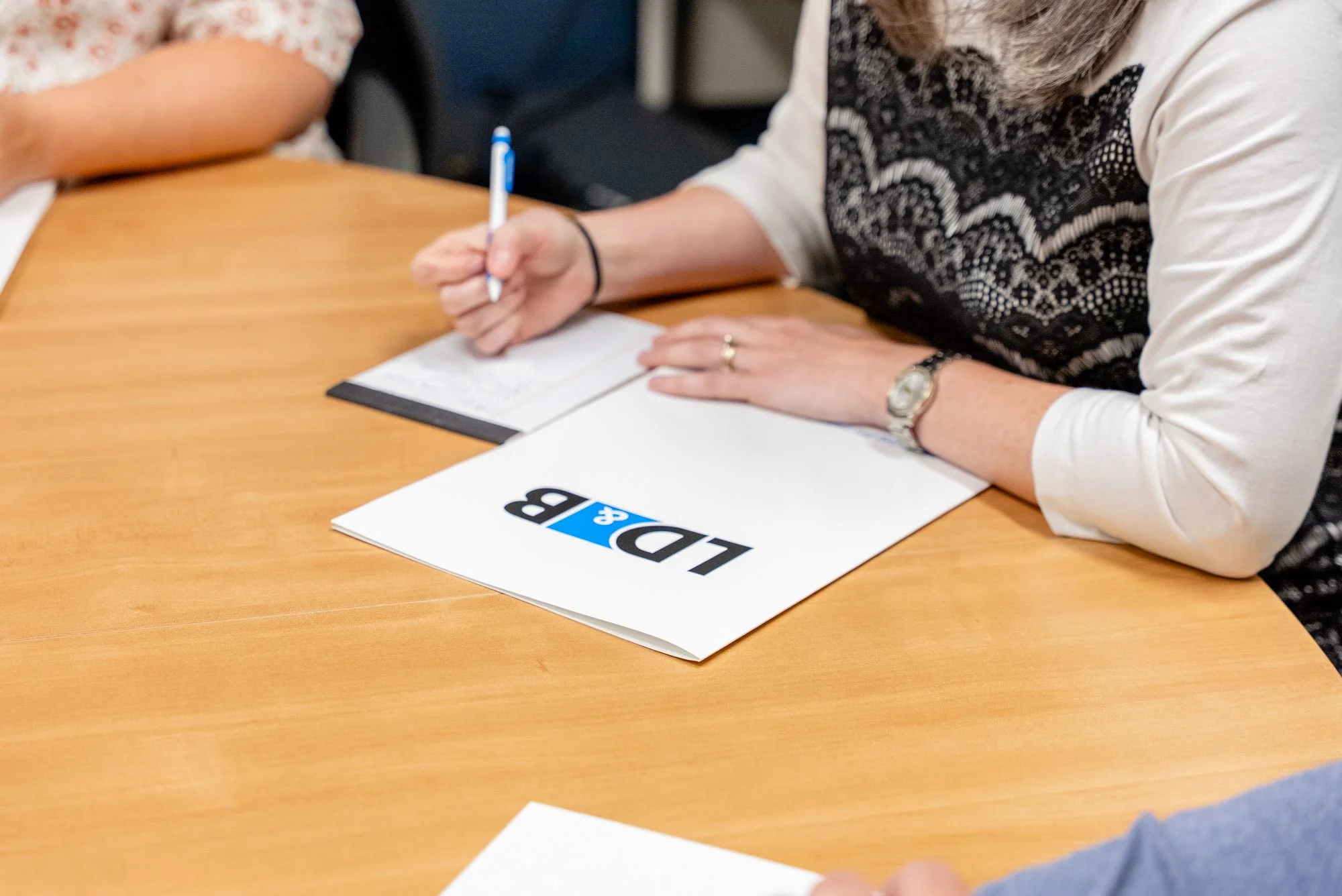 Person taking notes during a meeting, with an 'ID&B' folder on the table.
