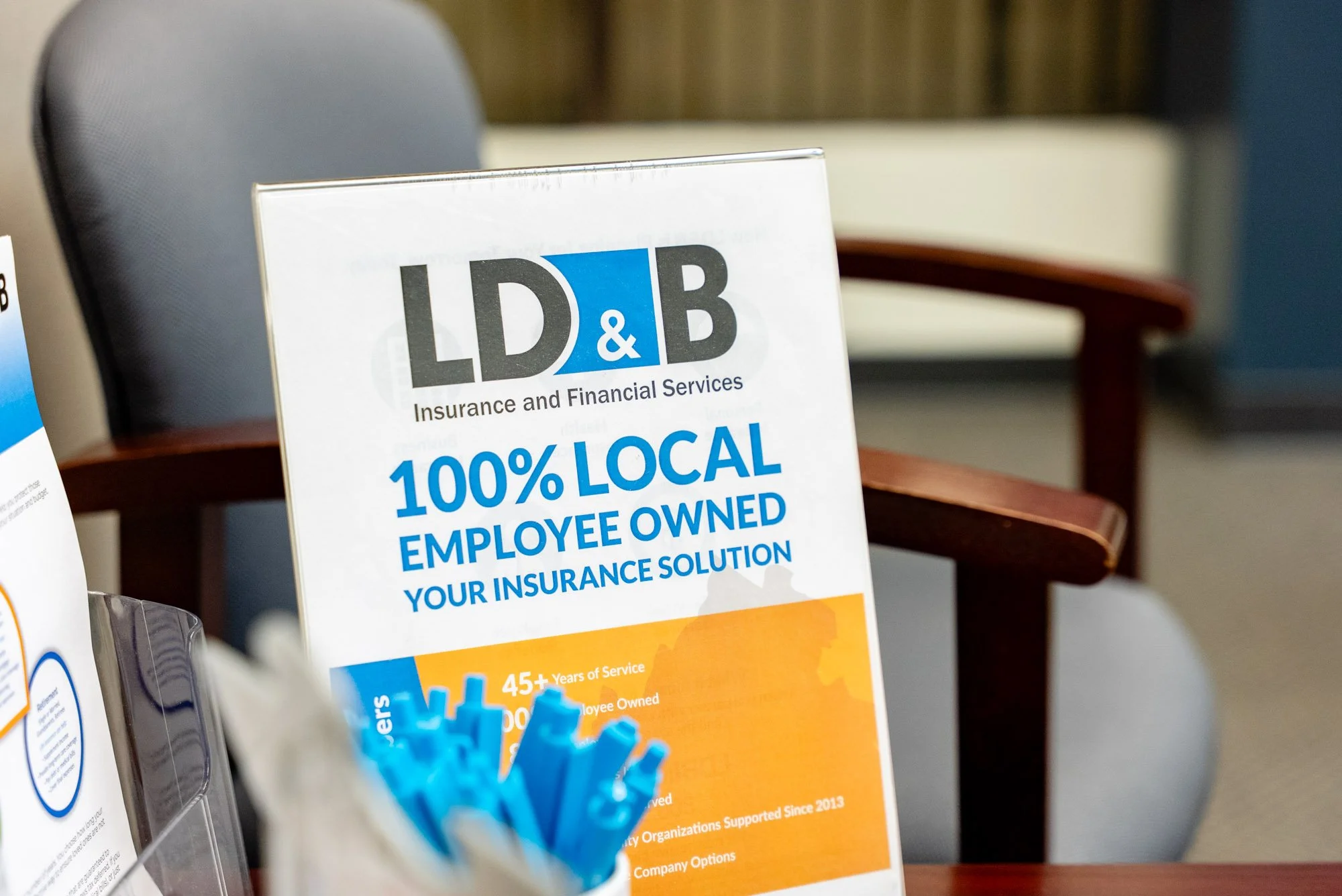 A LD&B Insurance and Financial Services brochure, highlighting its status as 100% local, employee owned with 45+ years of service, placed on a table in an office waiting area.