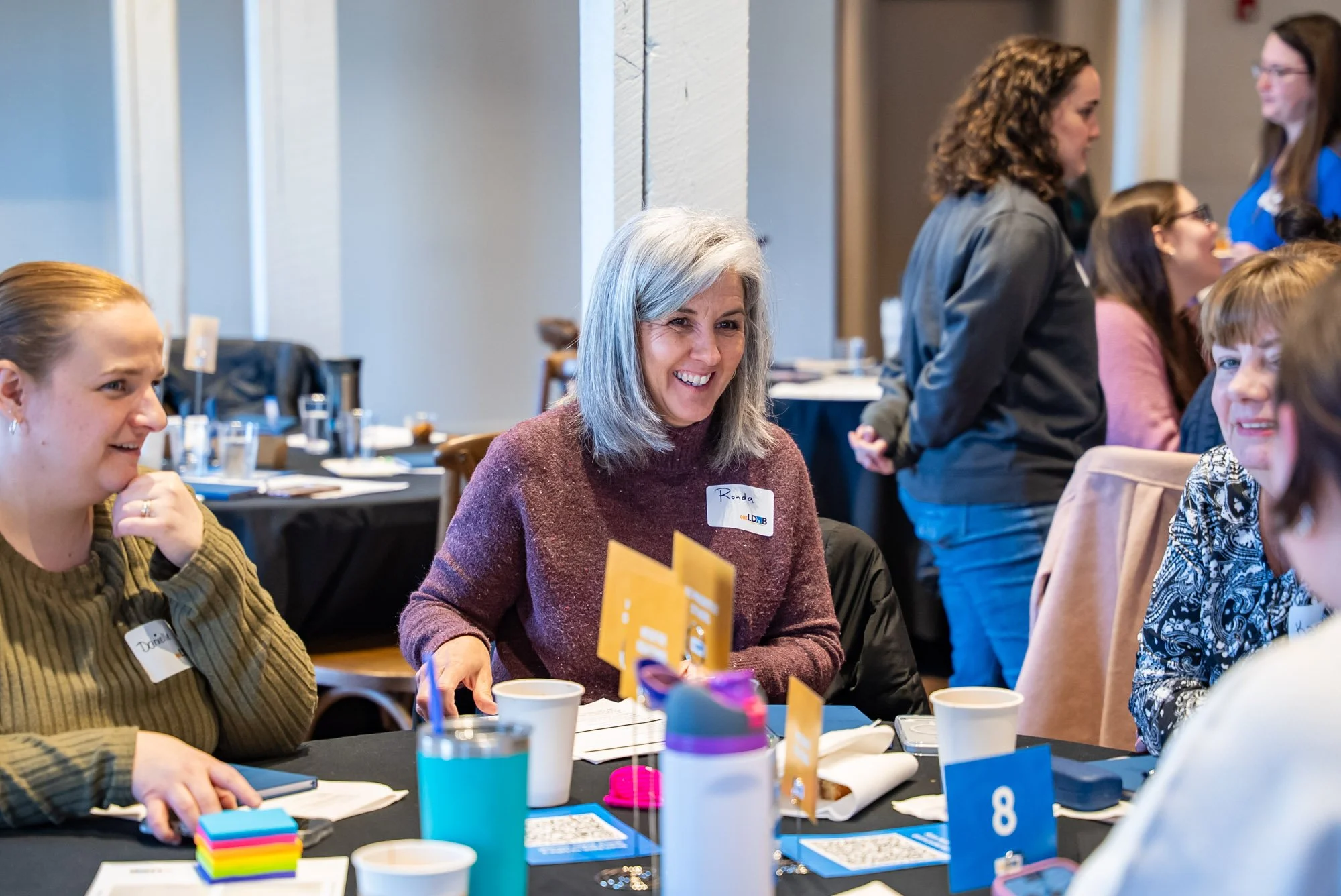 Groups of women talking and smiling at a round table during a conference or workshop.
