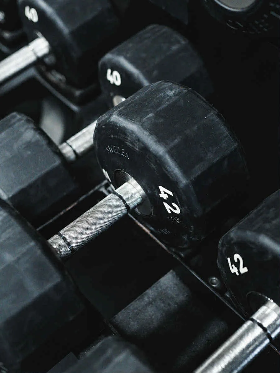 Nærbilde av håndvekter med vektangivelse, 42 kg, 40 kg og 42 kg, plassert på en vektstang.
