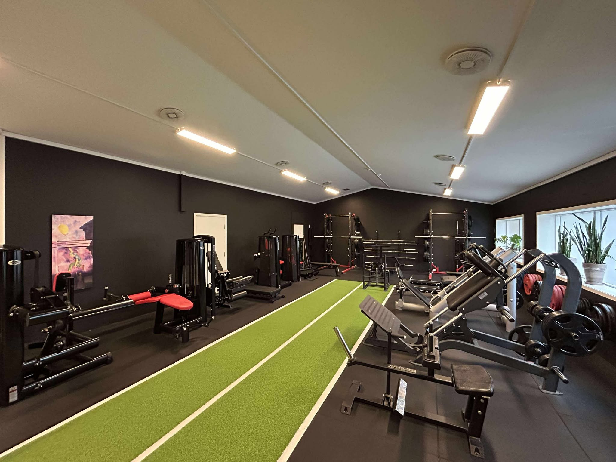 Innendørs treningsrom med ulike treningsapparater, vektstenger og løpebane fra Gym 80, Hammer Strength og Gymleco