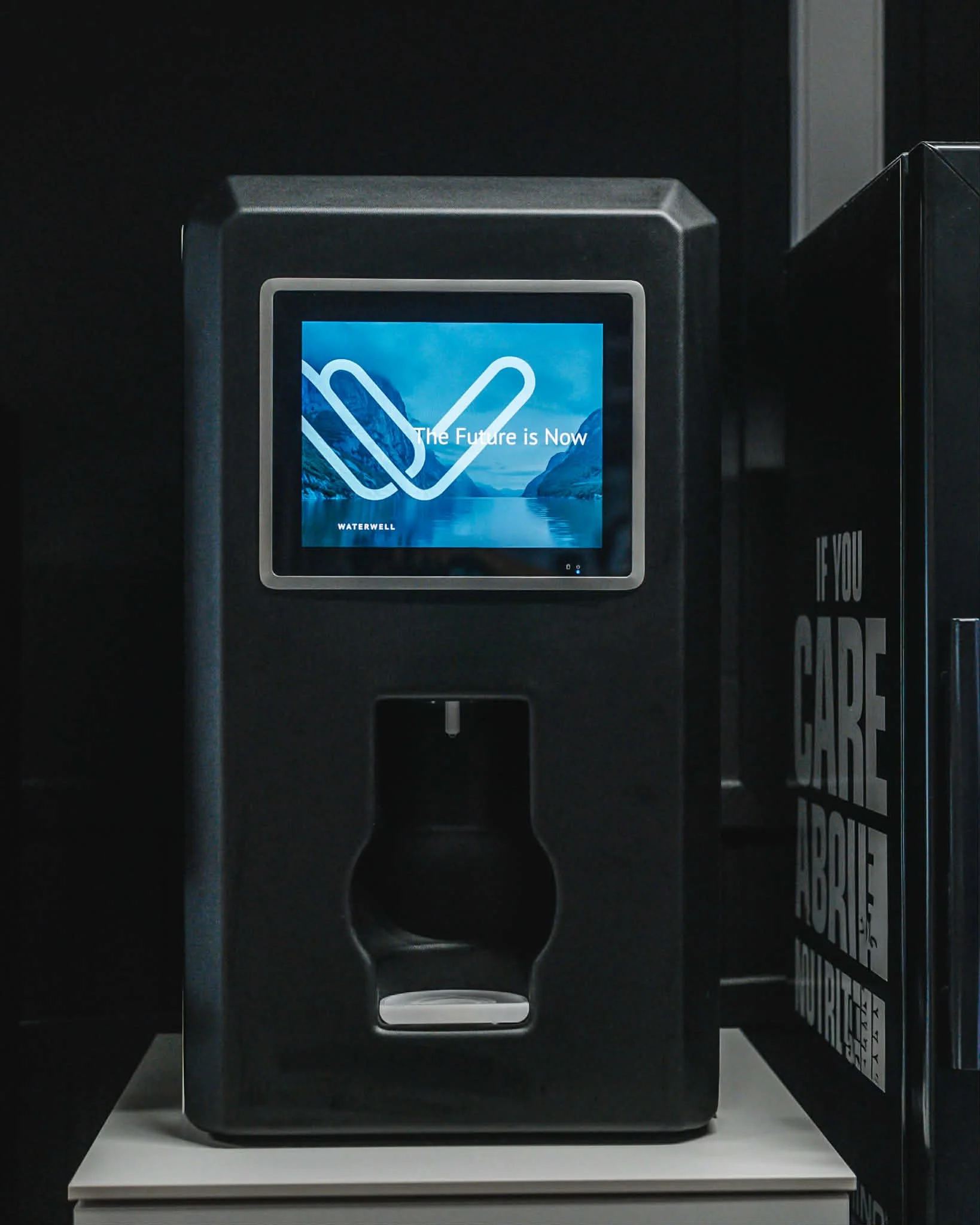 En svart vannautomat med en digital skjerm som viser et landskap og teksten 'The Future is Now'.