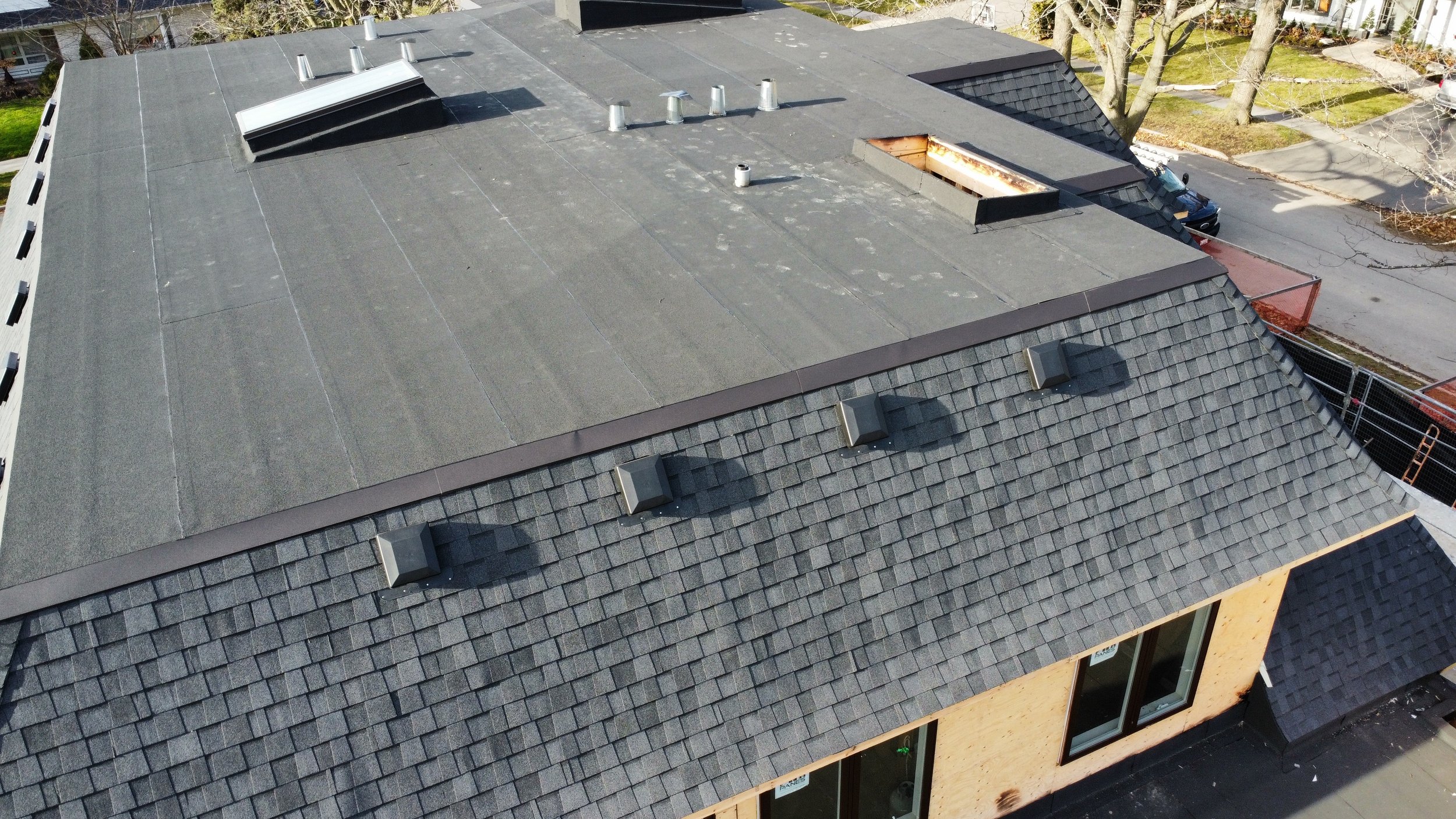 Aerial view of a house roof with multiple vents, a skylight, asphalt shingles, a two ply modified bitumen flat roof