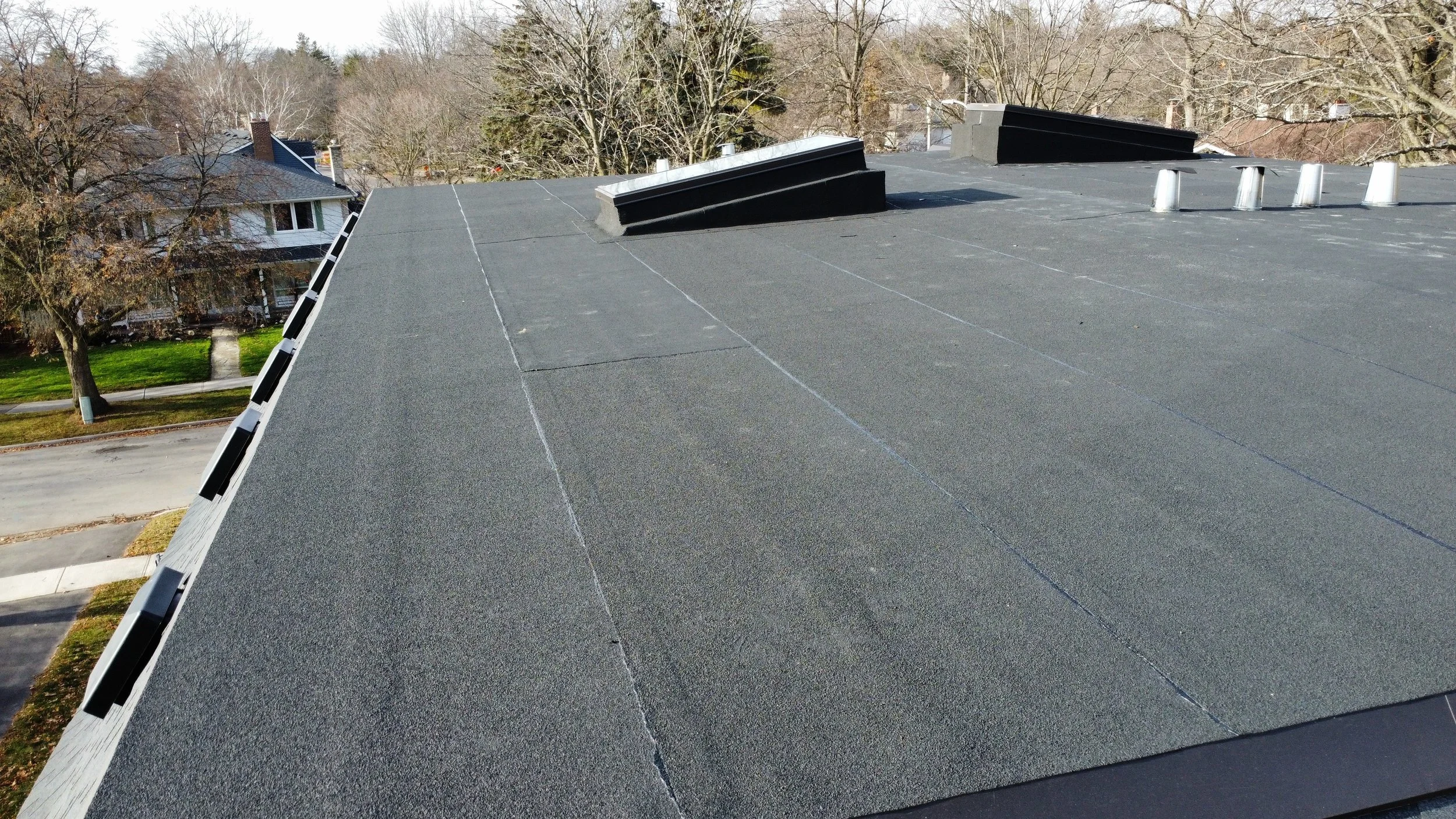 Aerial view of a house roof with multiple vents, a skylight, asphalt shingles, a two ply modified bitumen flat roof