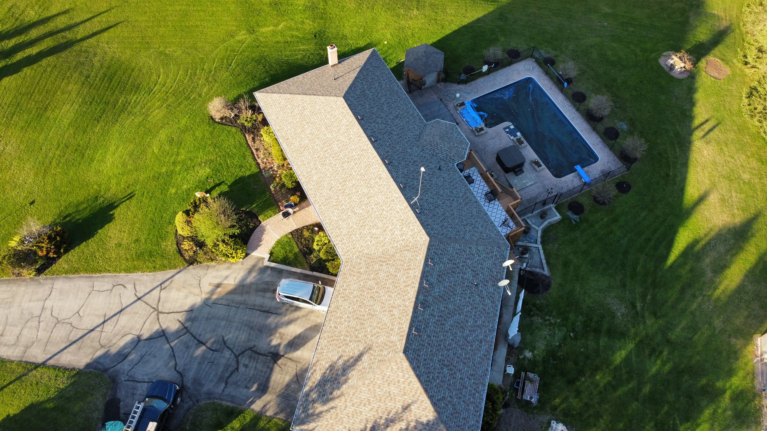 Aerial view of a house we installed asphalt shingles on with a large backyard, swimming pool, and driveway with parked vehicles.