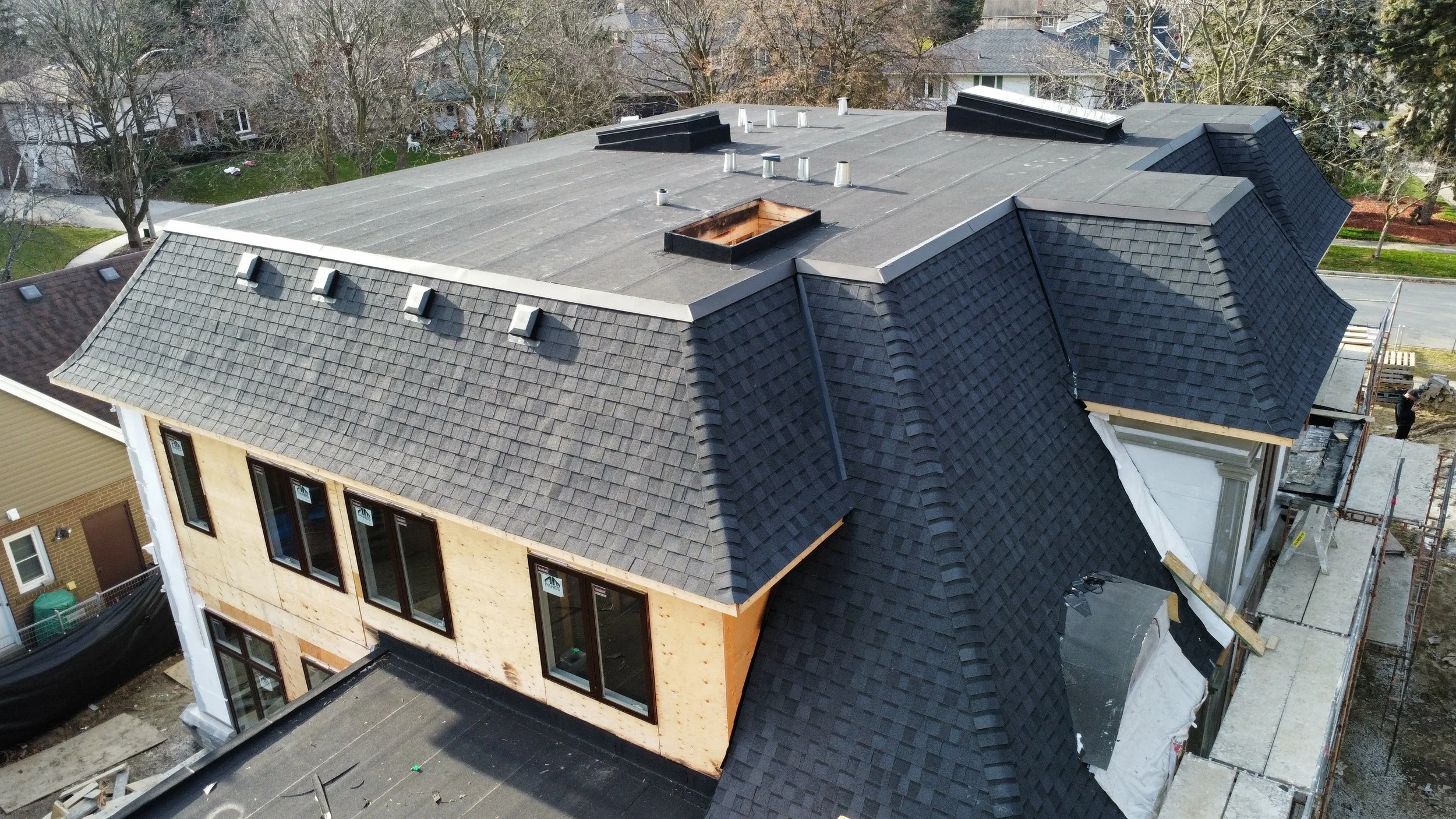 Aerial view of a house roof with multiple vents, a skylight, asphalt shingles, a two ply modified bitumen flat roof