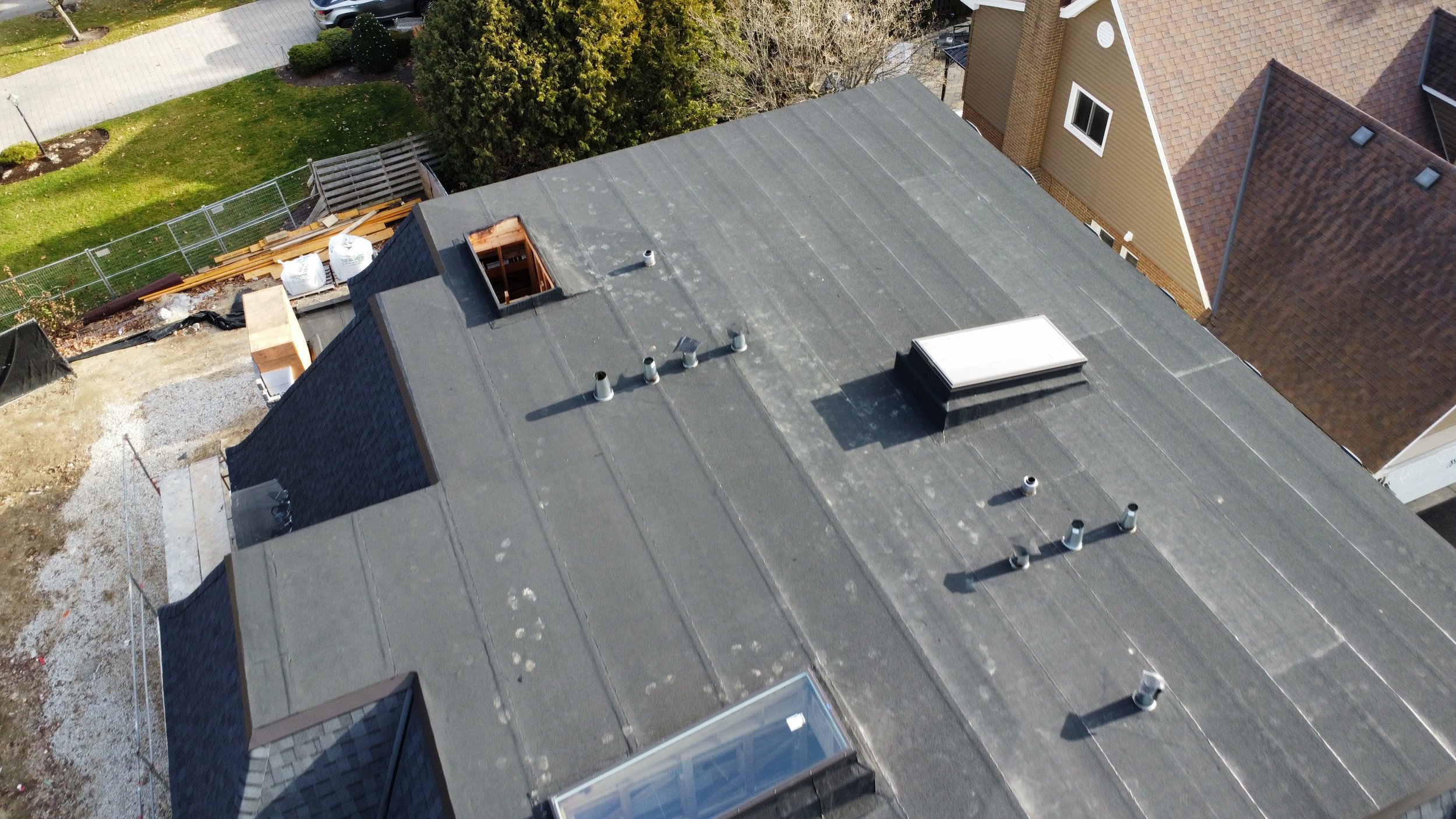 Aerial view of a house roof with multiple vents, a skylight, asphalt shingles, a two ply modified bitumen flat roof