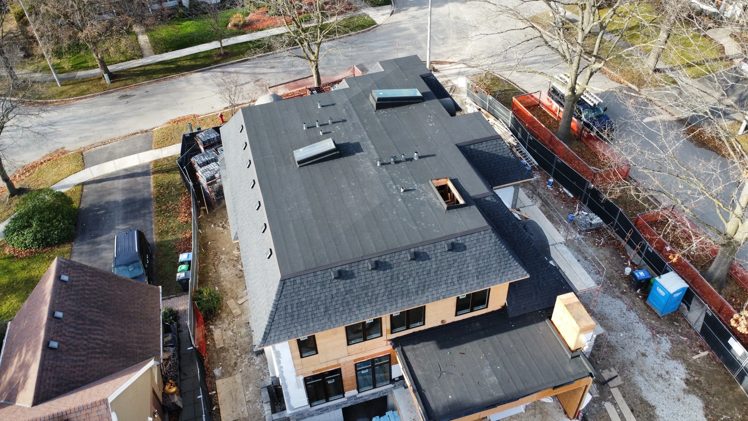 Aerial view of a house roof with multiple vents, a skylight, asphalt shingles, a two ply modified bitumen flat roof