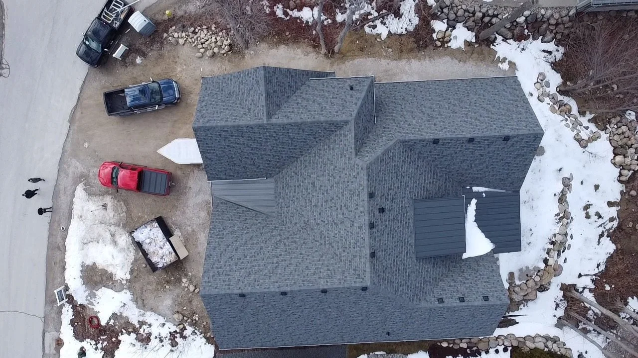 An aerial view of a house with a asphalt shingle and 24 gauge standing seam metal roof