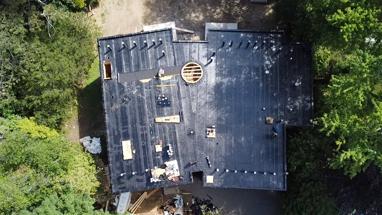 Aerial view of a house roof under construction, being installed is a 2ply modified bitumen flat roof system