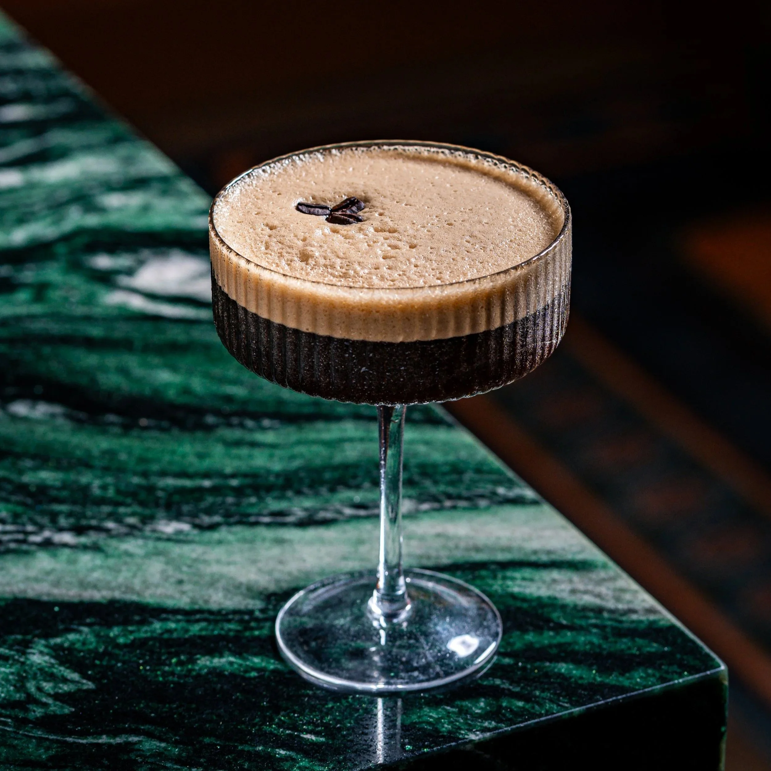 A coffee cocktail with a frothy top and a few coffee beans garnishing, served in a coupe glass.