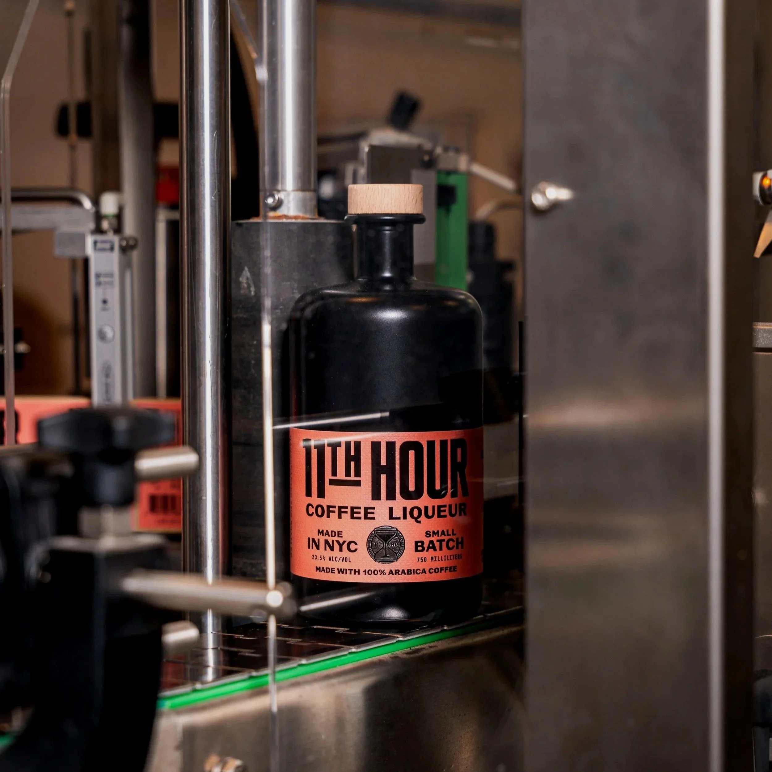 A black bottle labeled '11TH HOUR COFFEE LIQUEUR' on a metal shelf in a commercial setting.