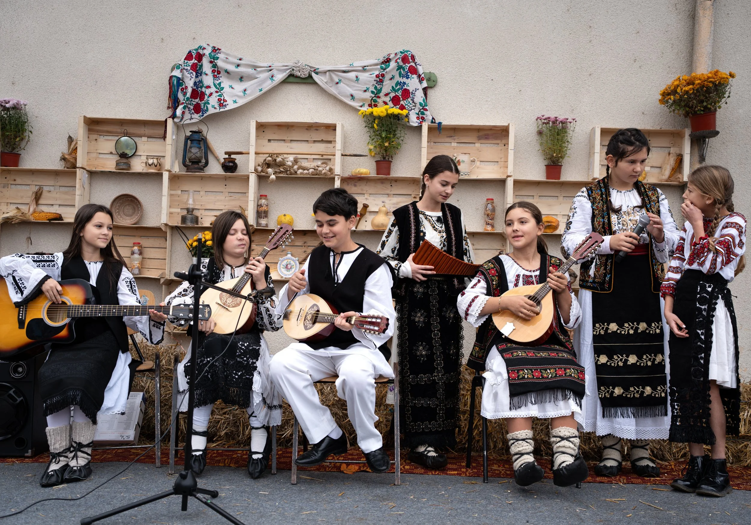 Group of children dressed in traditional folk costumes, some playing guitars and a zithers, on stage during a cultural performance.