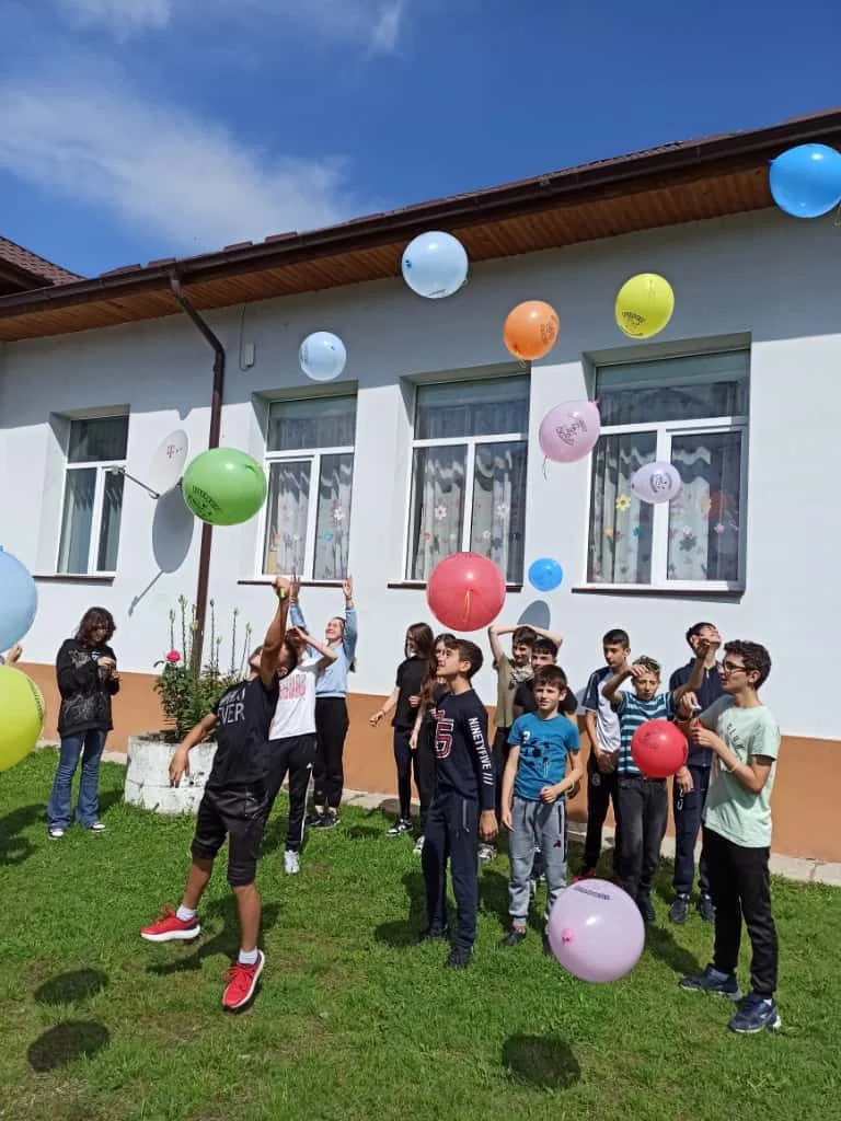 A group of children outside a house releasing colorful balloons into the sky.