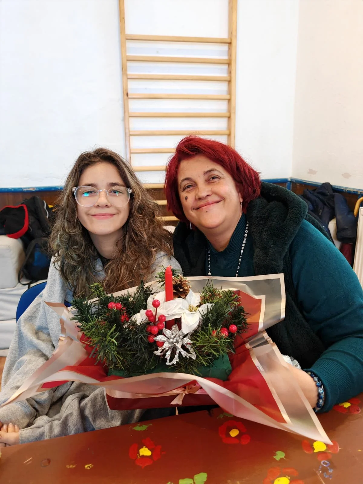 Two smiling women sitting at a table with a decorated Christmas centerpiece, surrounded by holiday decorations, in a room with a climbing wall in the background.