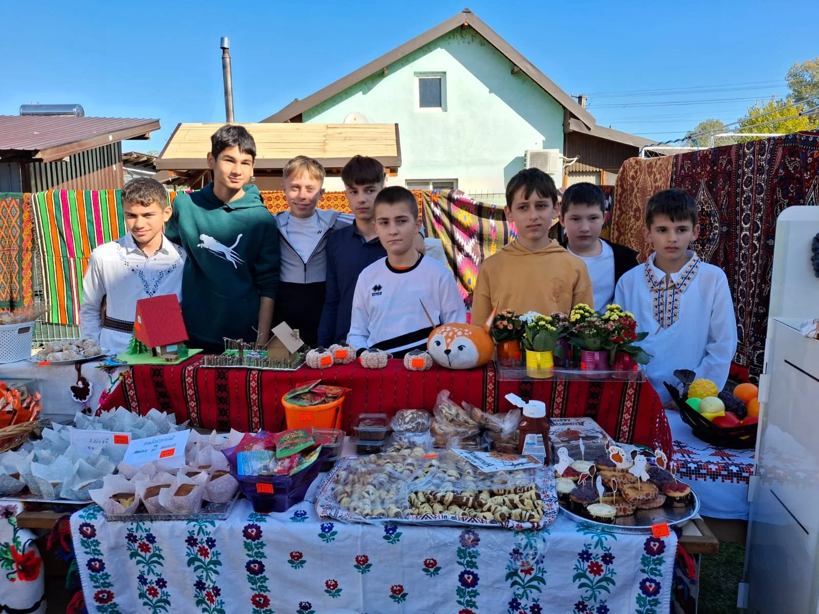 Group of boys standing behind decorated tables with baked goods and crafts at an outdoor event.