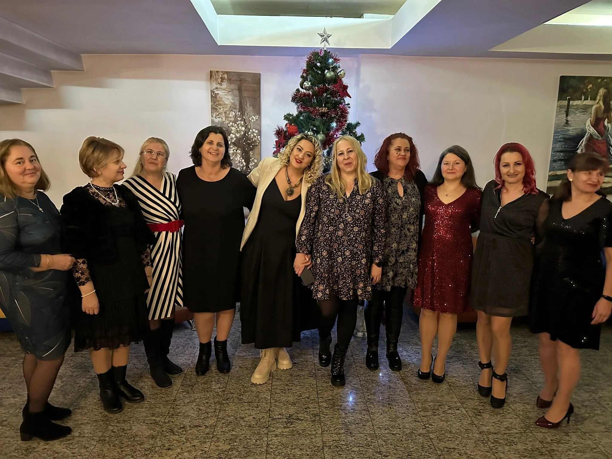 Group of women standing together in front of a decorated Christmas tree, indoors, celebrating a holiday party.