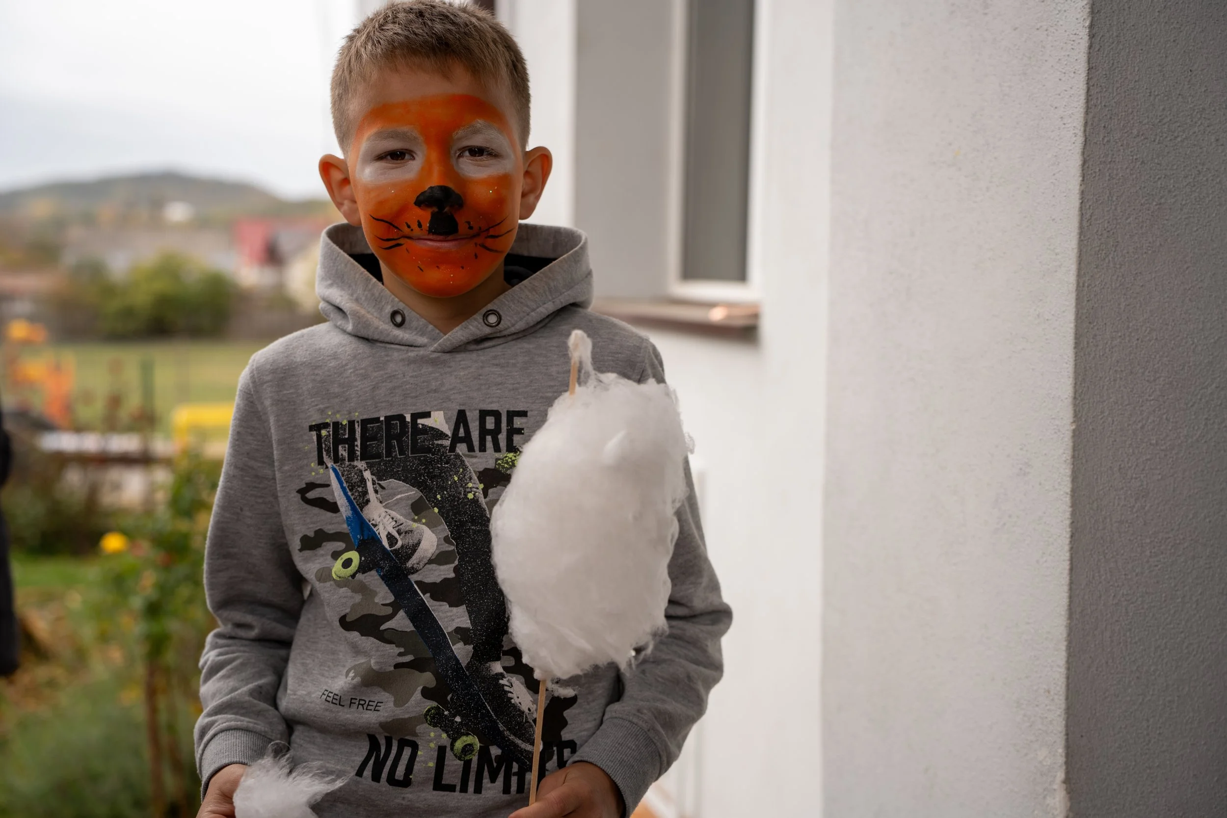 A boy with a painted face resembling a tiger holding a stick with cotton candy.