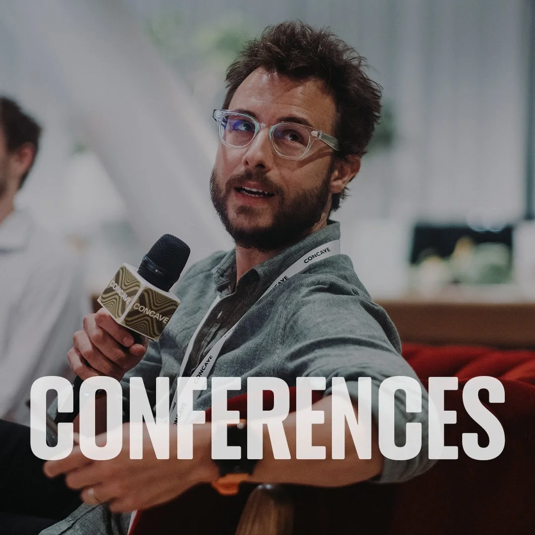A man with glasses and a beard holding a microphone during a conference, with the word 'CONFERENCES' overlayed at the bottom.