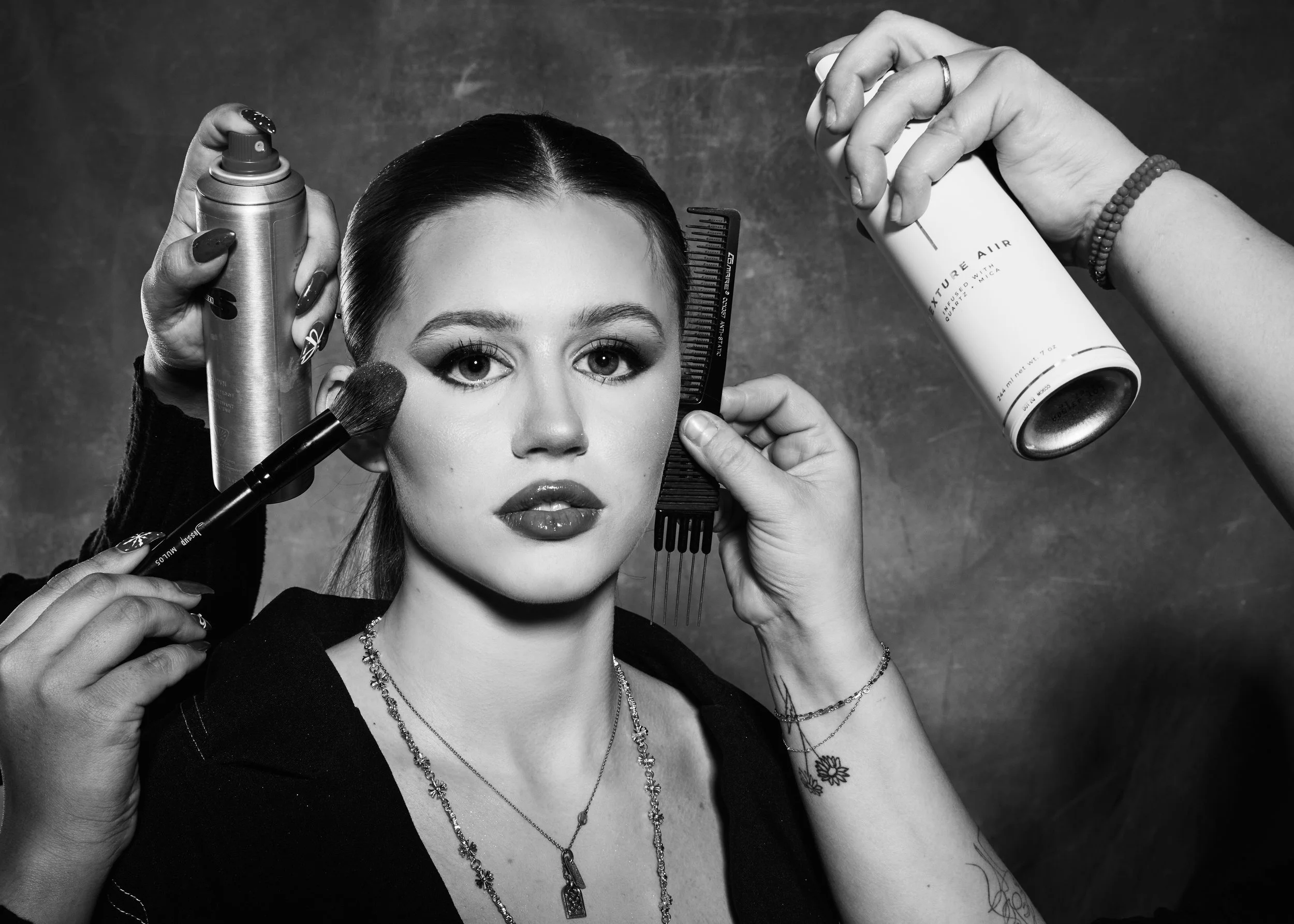 Black and white photo of a woman with makeup artists applying makeup and styling her hair.