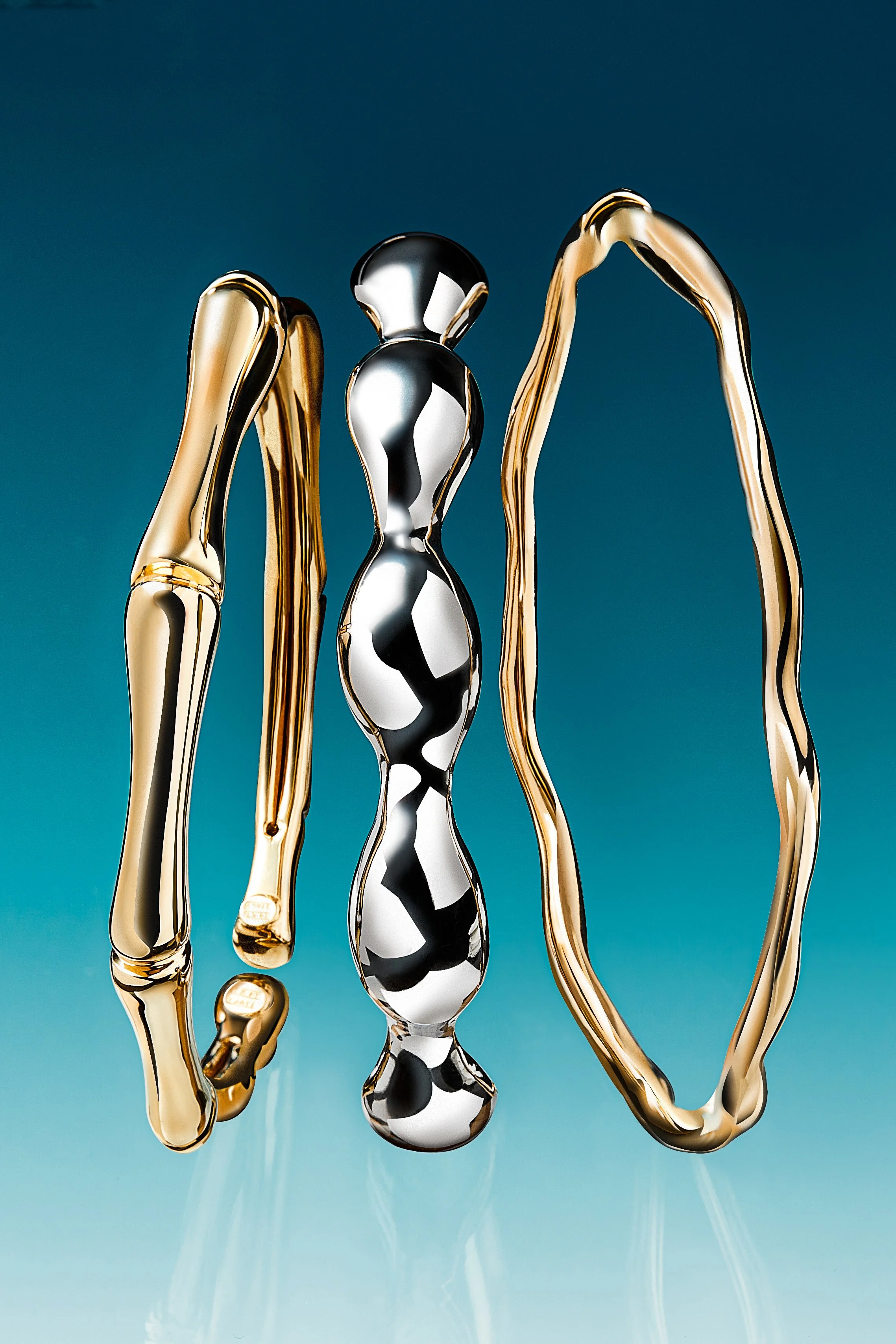 A set of three metallic abstract sculptures, one gold, one silver, and one gold with a looping shape, displayed against a blue background.