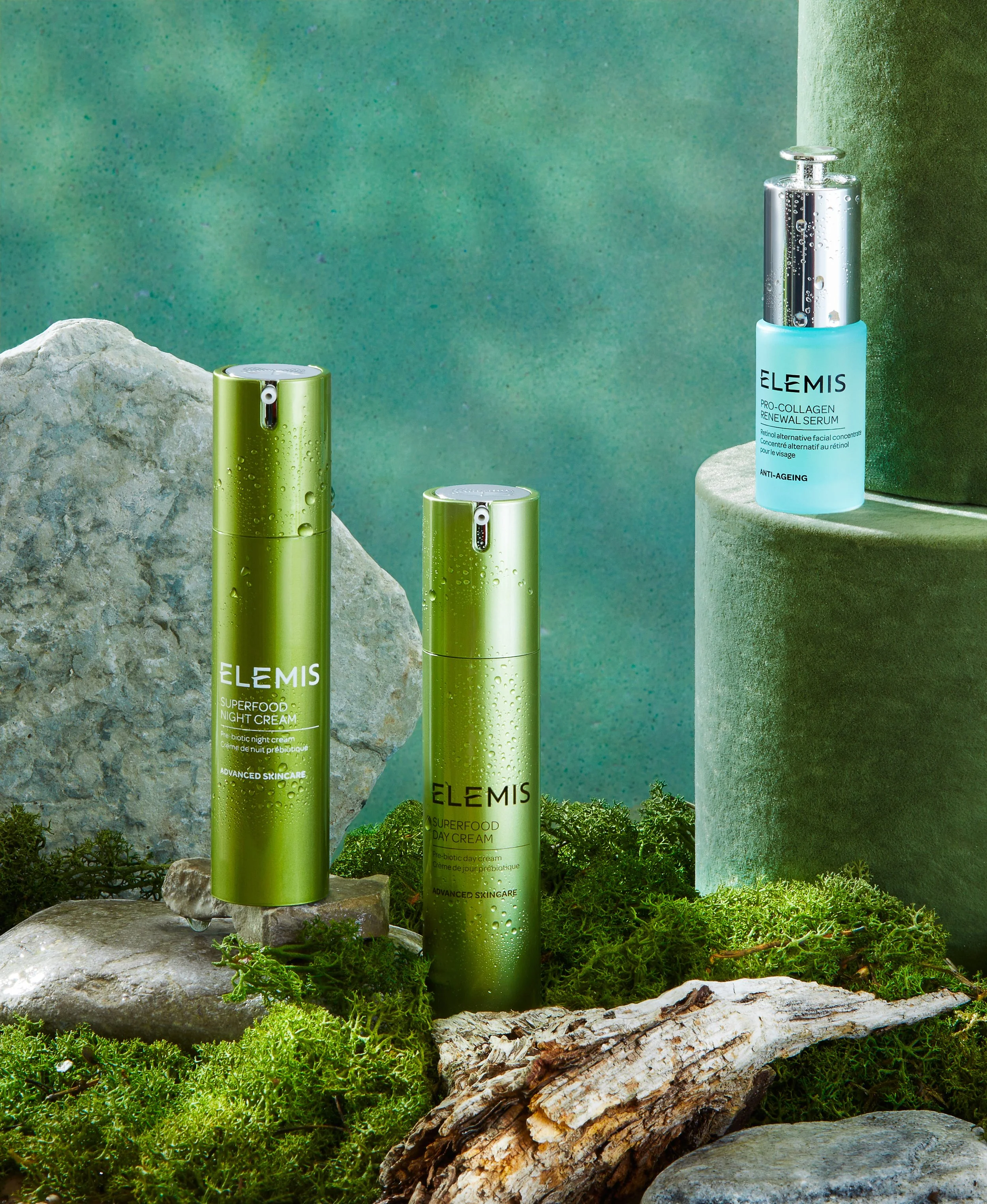 Skincare products from Elemis, including night cream, day cream, and serum, displayed on moss and stones with a green background.